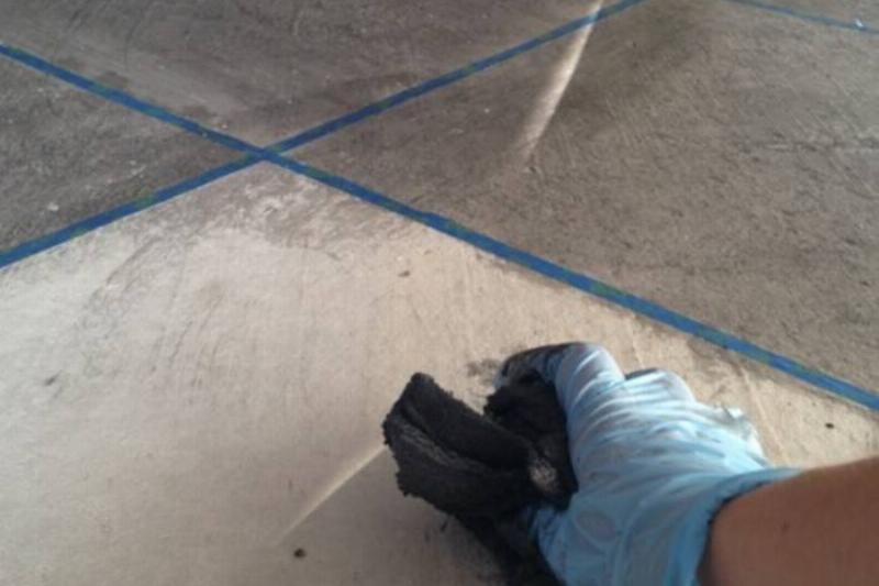 Gloved hand applying stain to concrete.