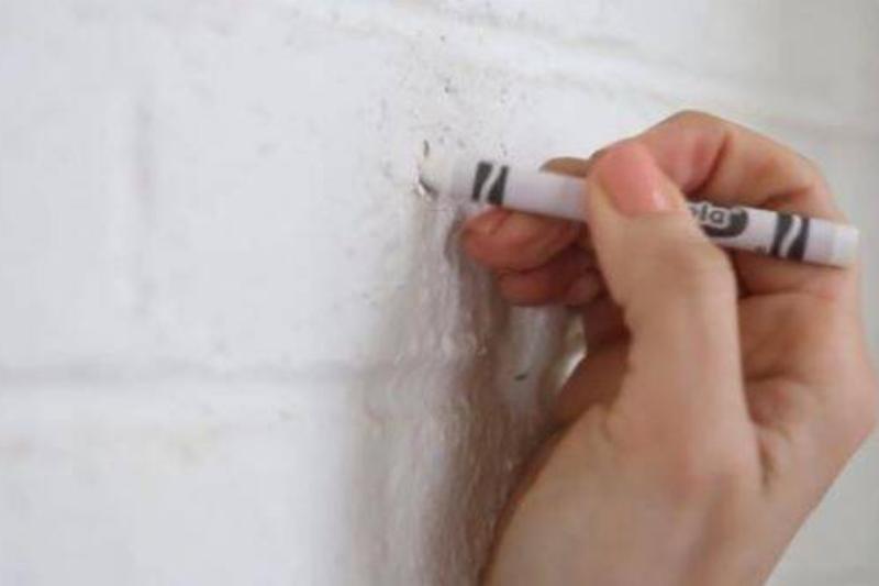 Using white crayon to fill hole in a wall.