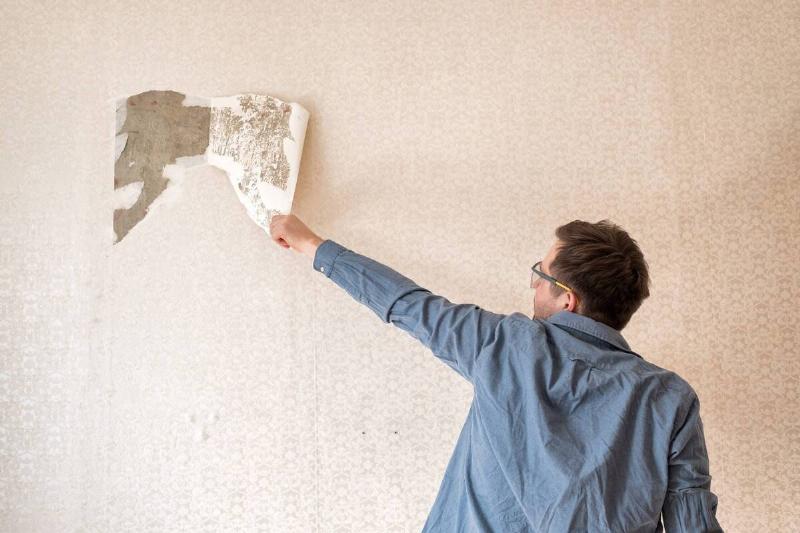 Man tearing wallpaper off a wall.