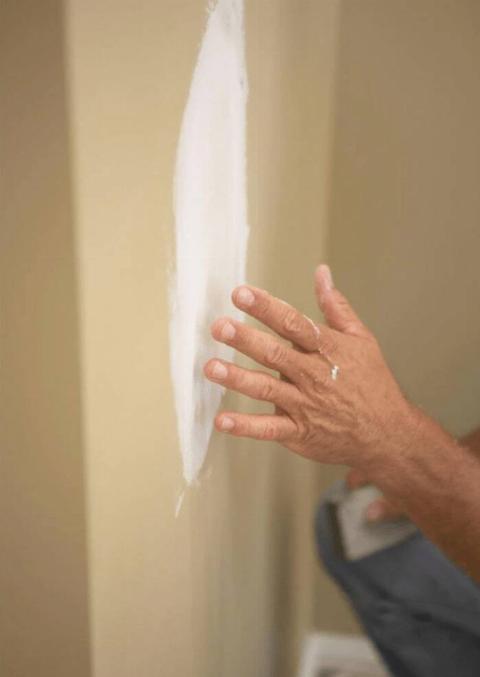 A hand over a repaired drywall section.