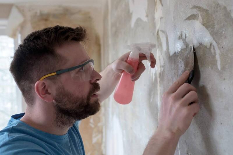 Man scraping off wallpaper. 