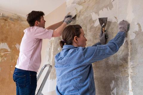 Two people removing wallpaper from a wall. 