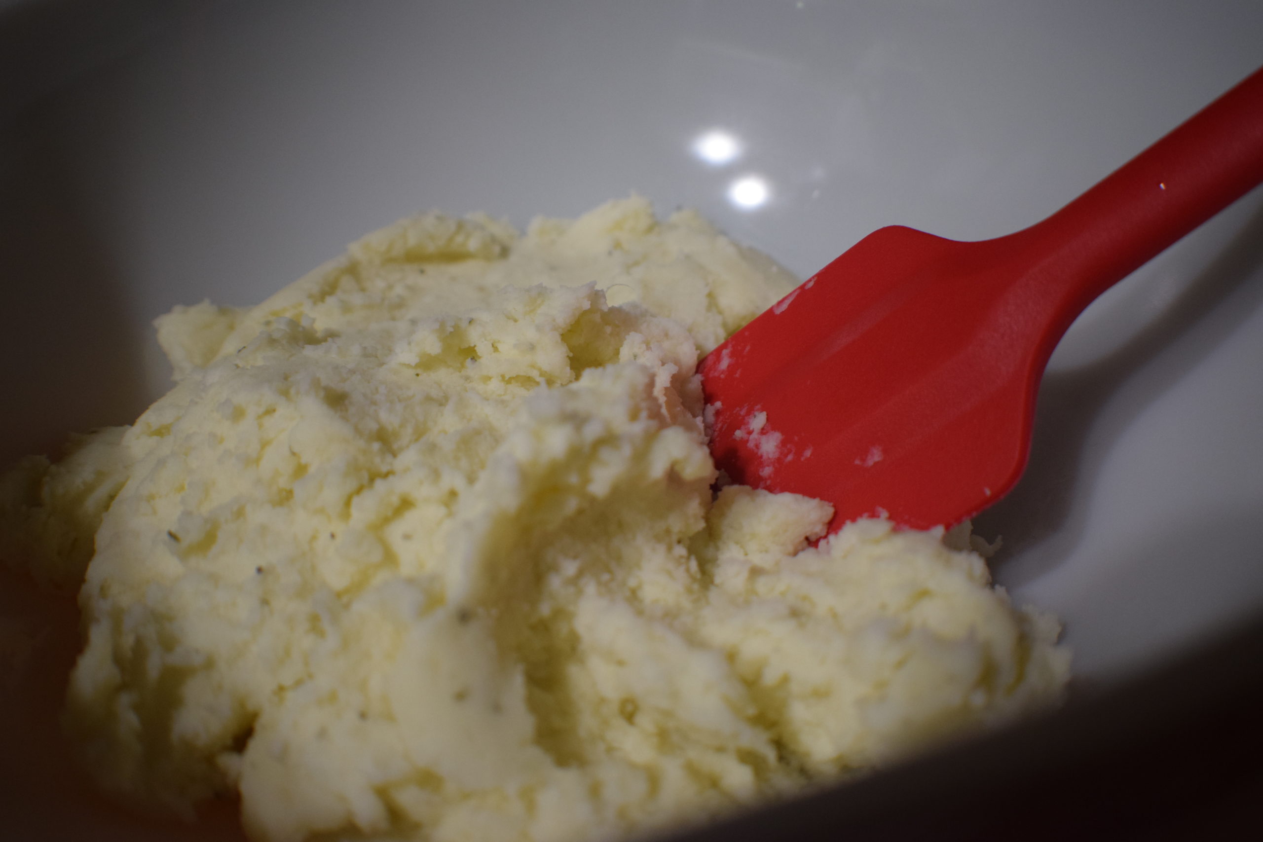 mashed potatoes in a white bowl with red spoon