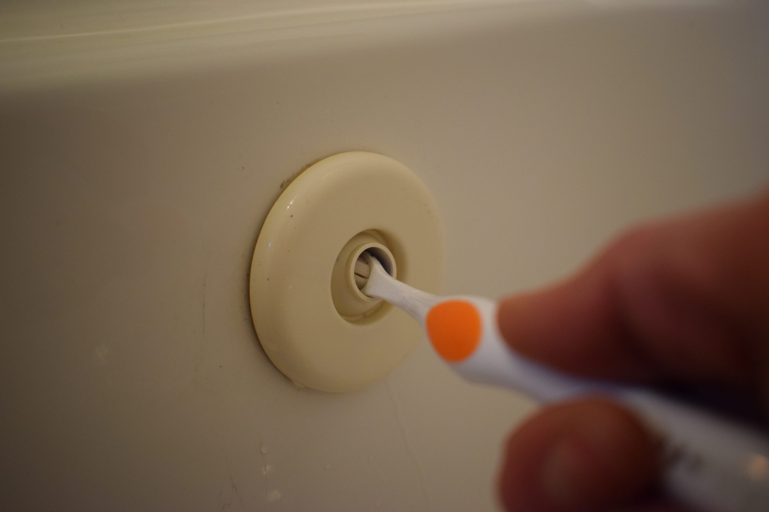 Orange toothbrush cleaning inside tub jet