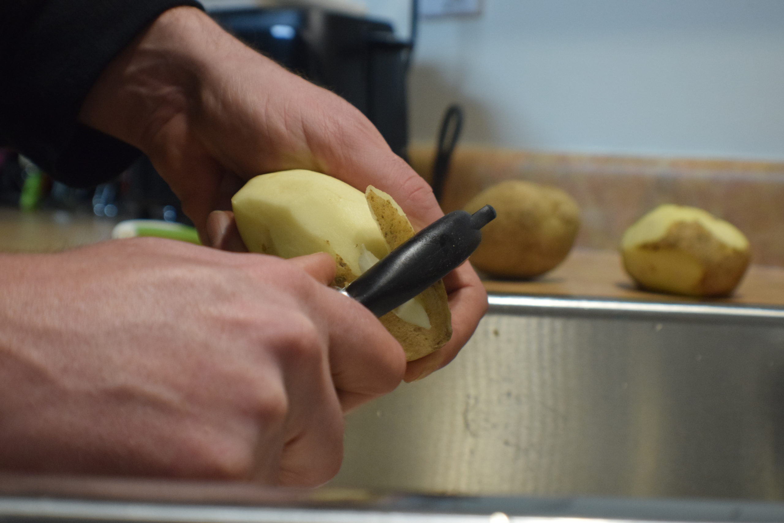 hands peeling potato in a sink with a potato holder