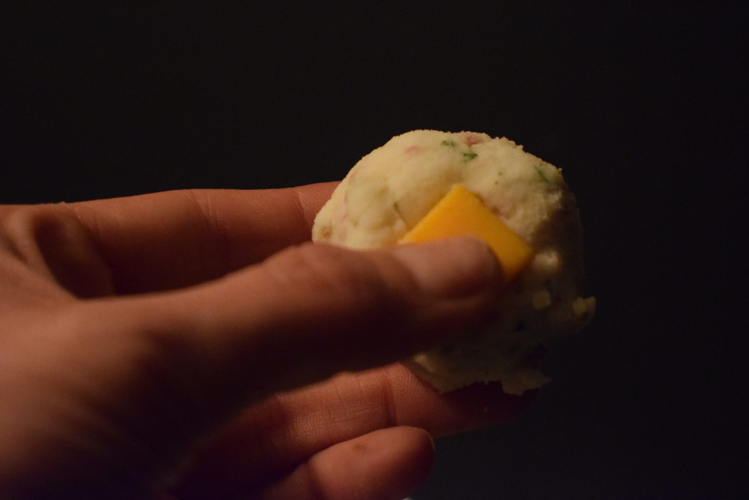 Thumb pushing cheddar cheese into mashed potato ball