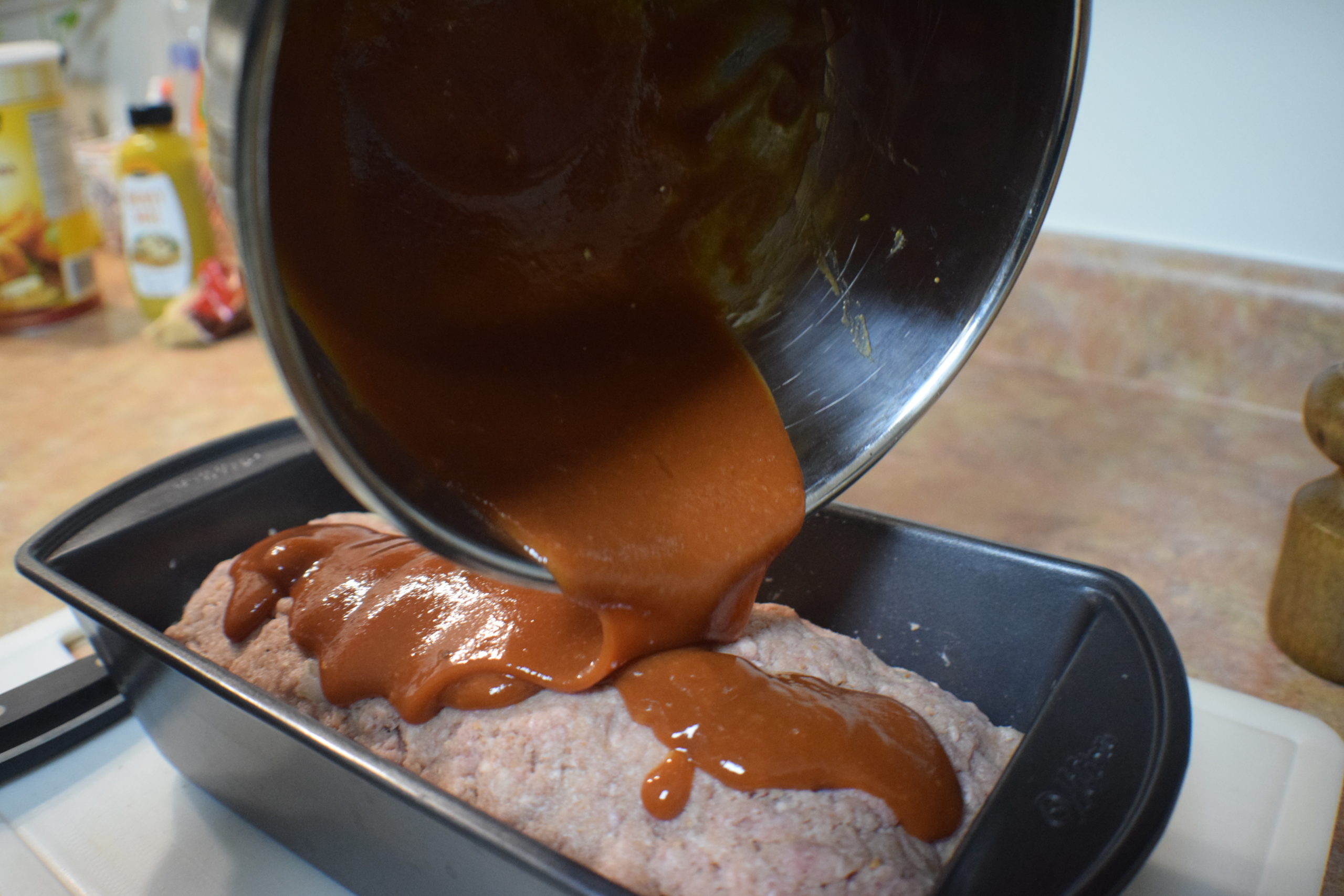 metal bowl pouring sauce on raw meatloaf