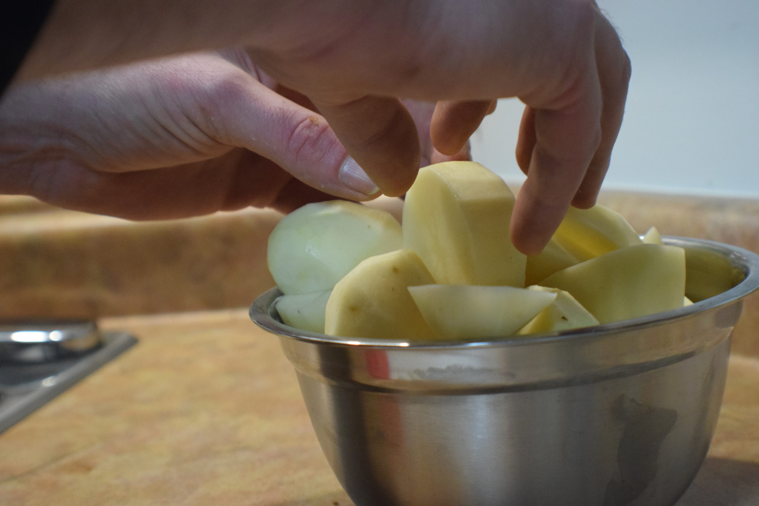 mans hands putting potatoes in a metal bowl