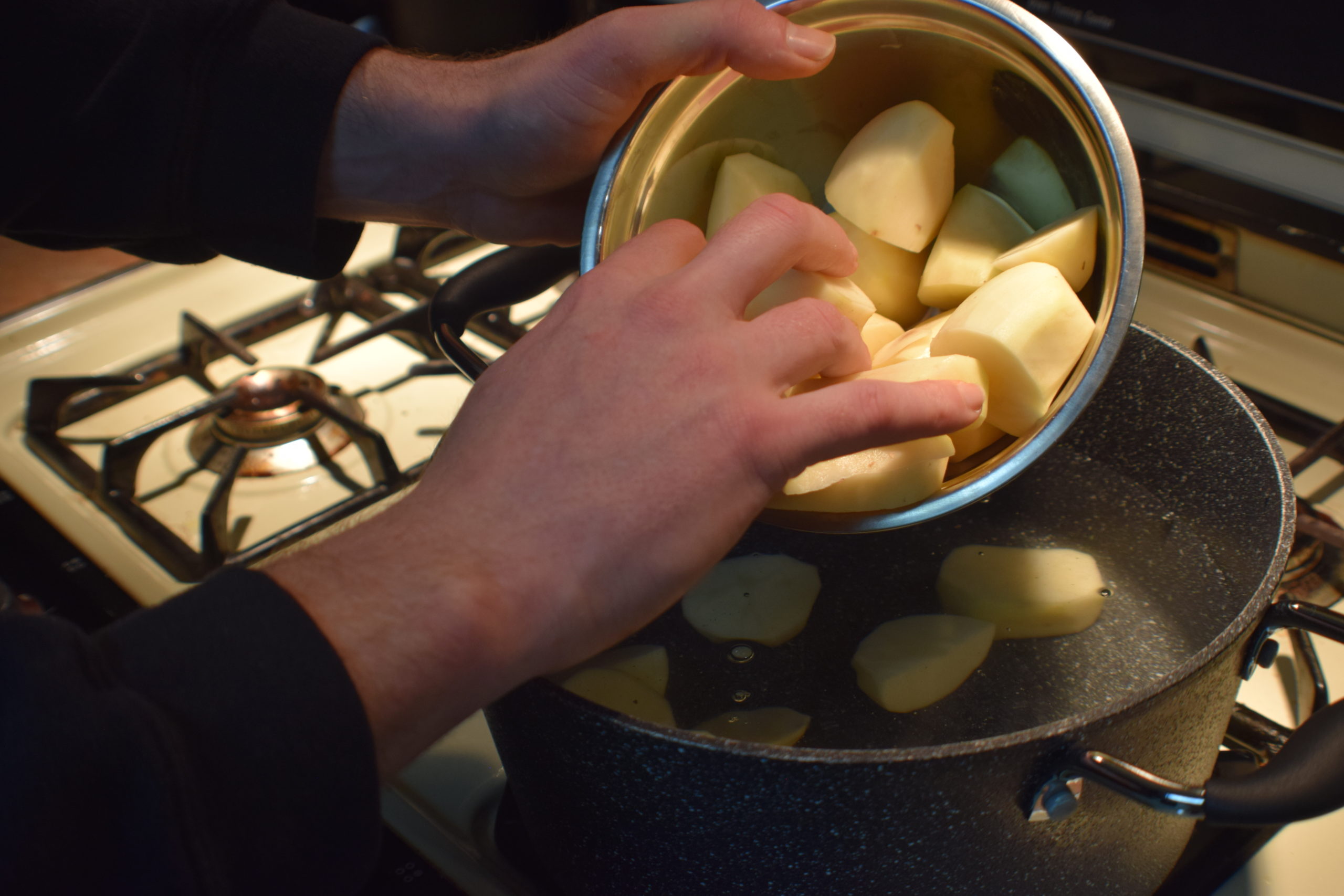 mans hands putting cut potatoes into a pot of water