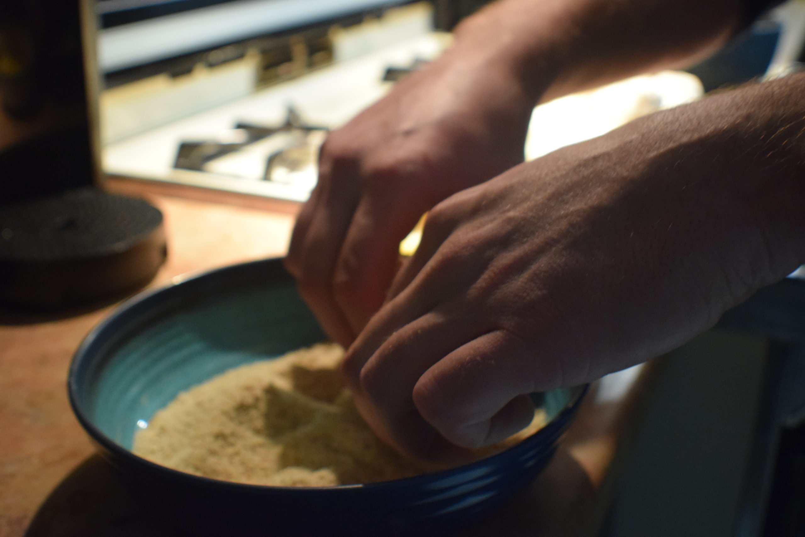 Man hands rolling food into breadcrumbs in a blue bowl