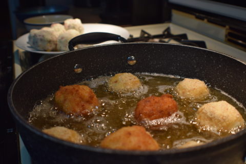 breaded potato balls cooking in hot oil on the stove