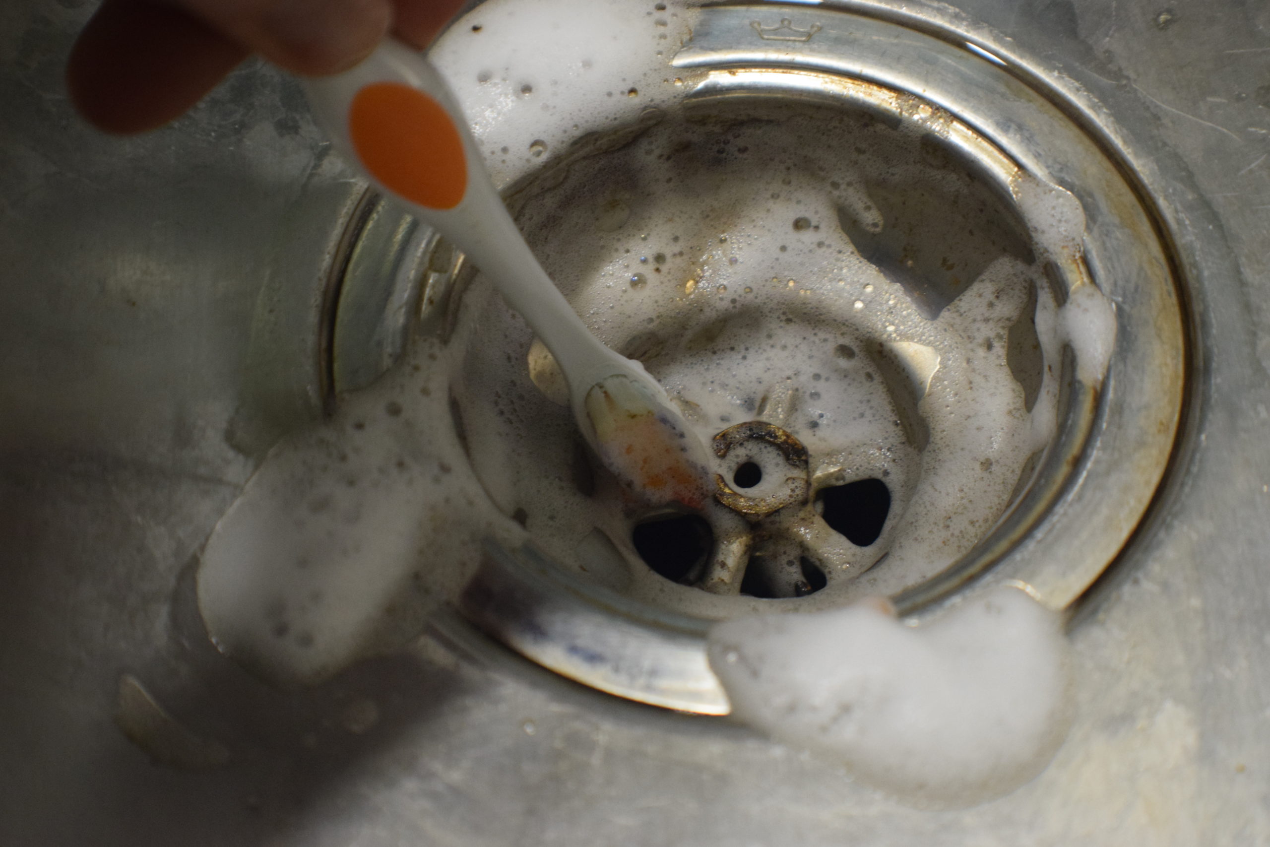 white and orange toothbrush cleaning metal sink strainer