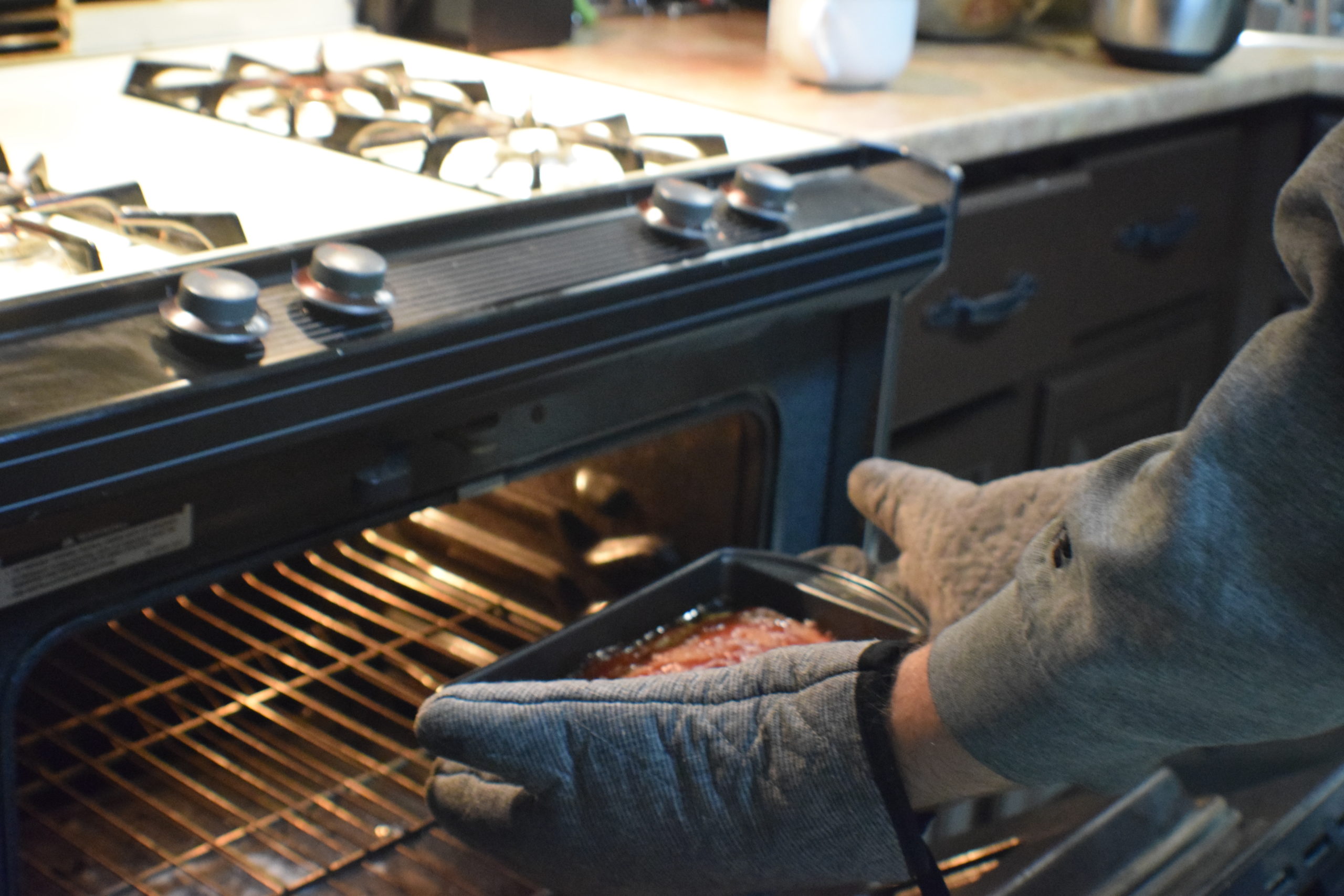 Man with grey striped oven mitts removing meatloaf from oven