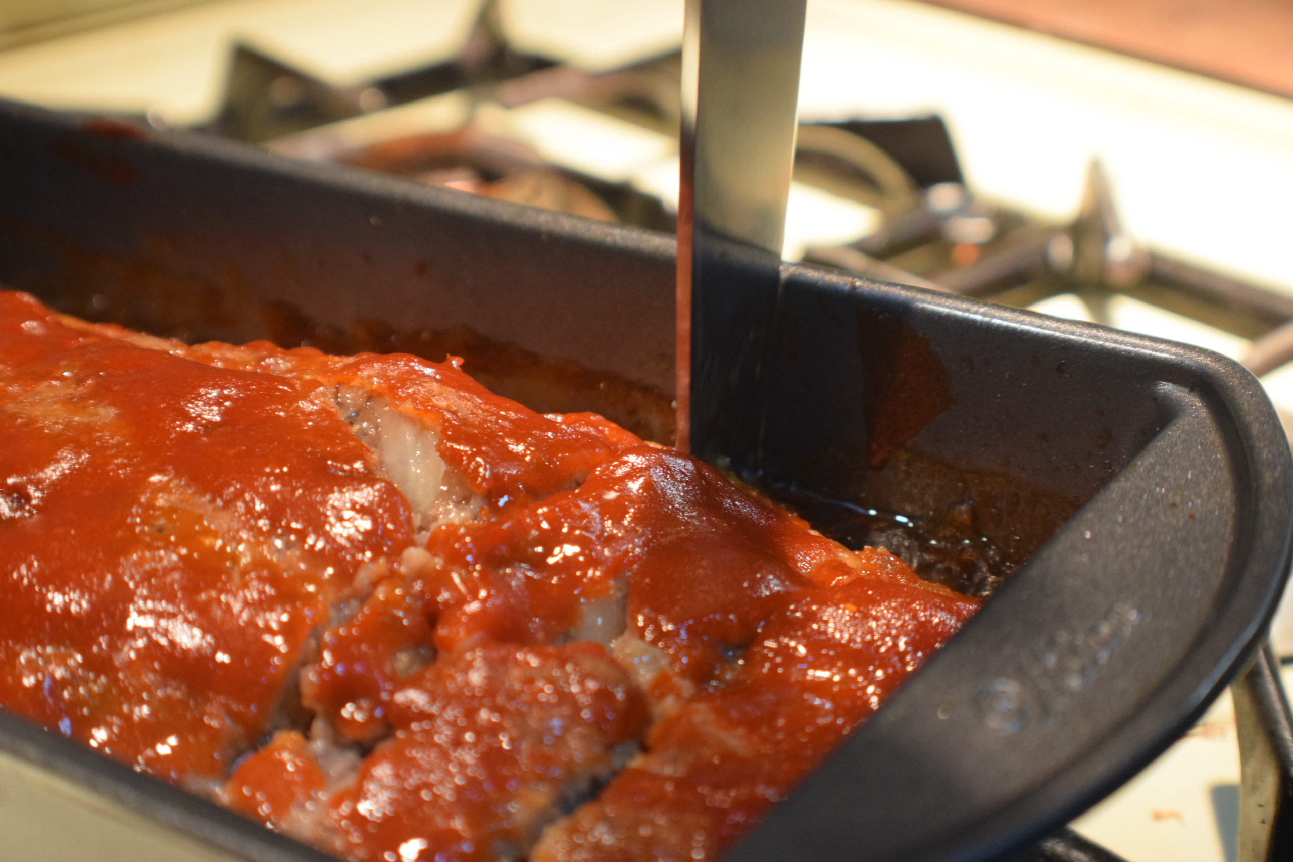 cooked meatloaf in pan being cut by a long knife