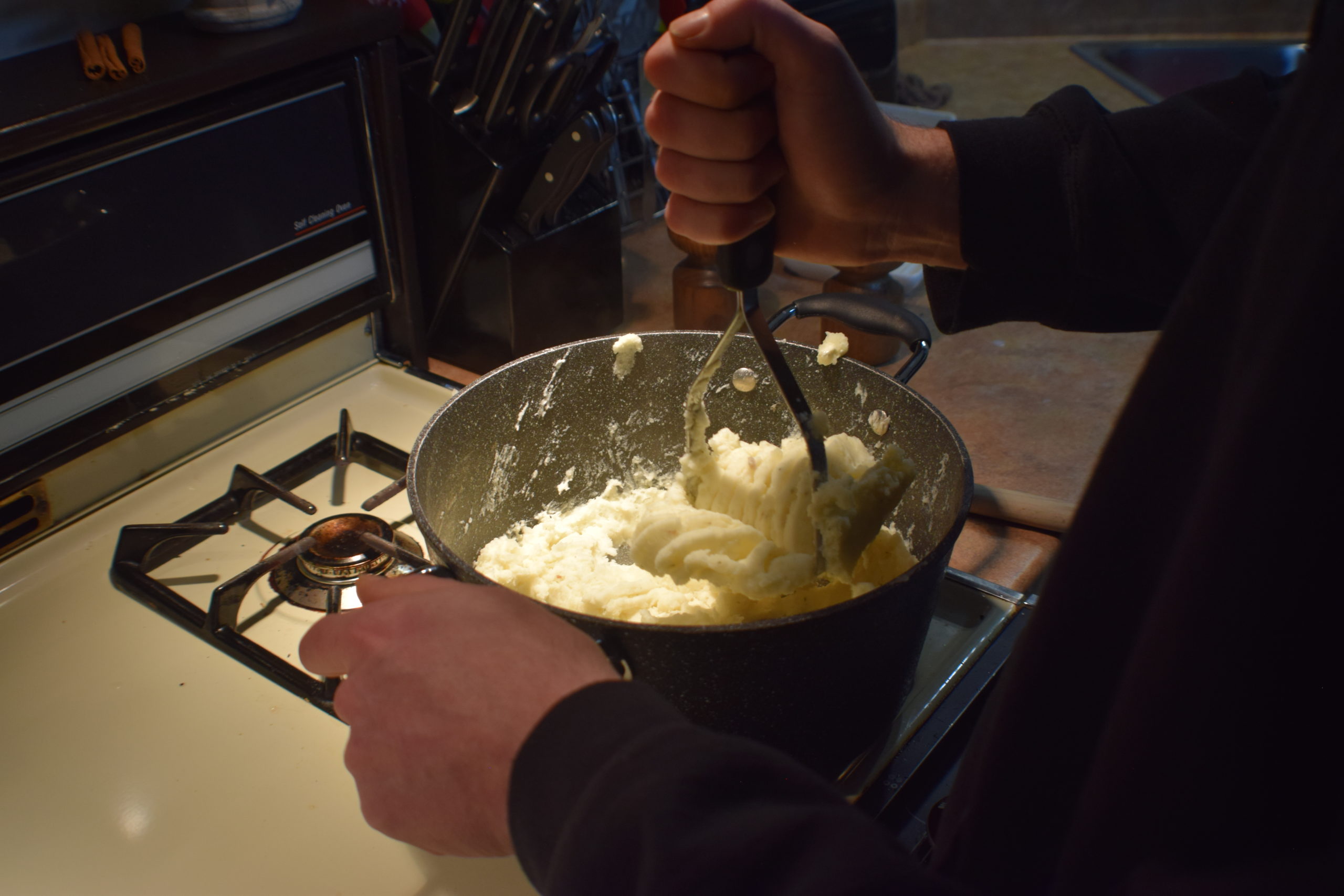 Man in sweater mashing potatoes with a potato masher