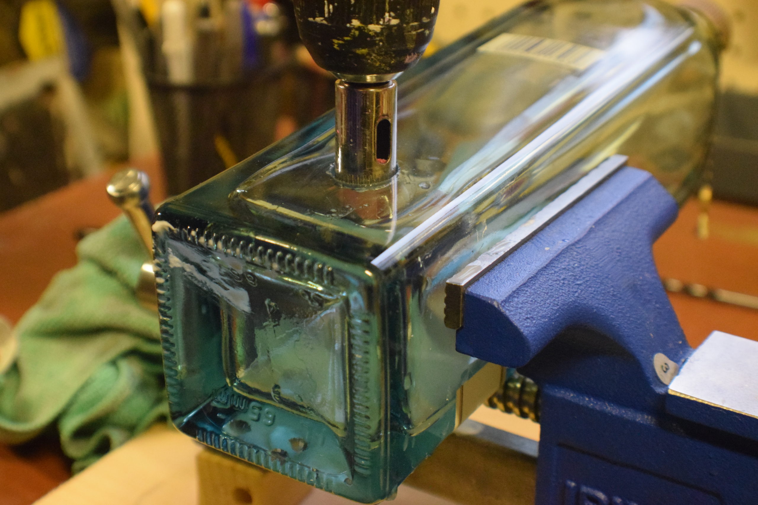 Diamond drill bit drilling through square liquor bottle on work bench