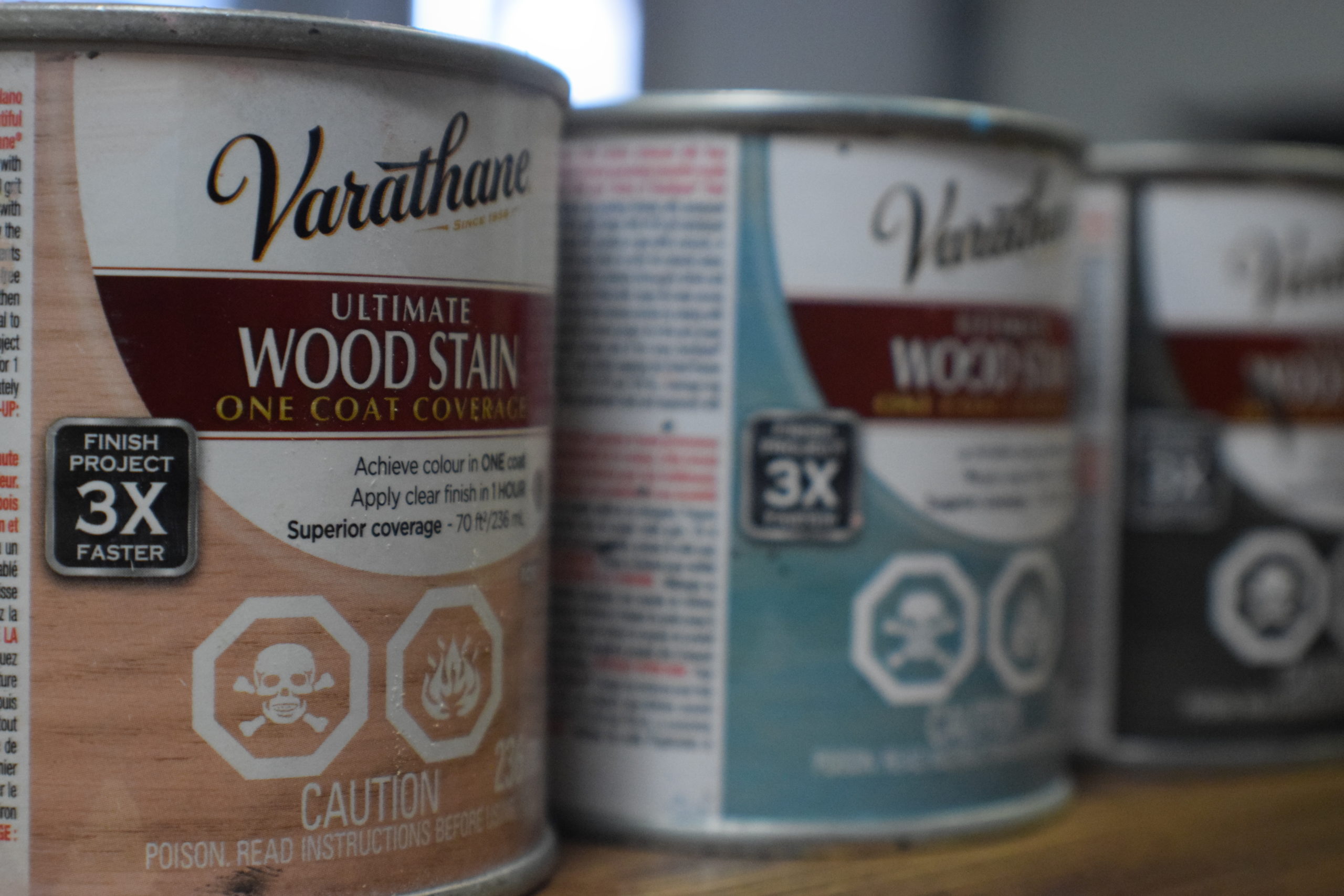 Varathane wood stain cans in pink, aqua and charcoal lined up on a table