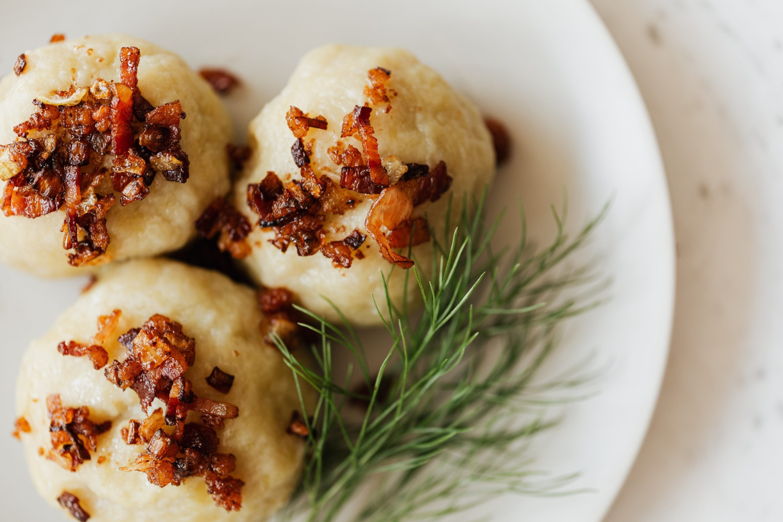 potato dimplings with bacon crumble and dill on white plate