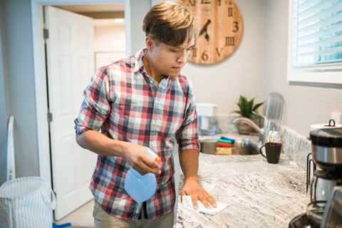 Asian man in checkered shirt washing a marble kitchen counter
