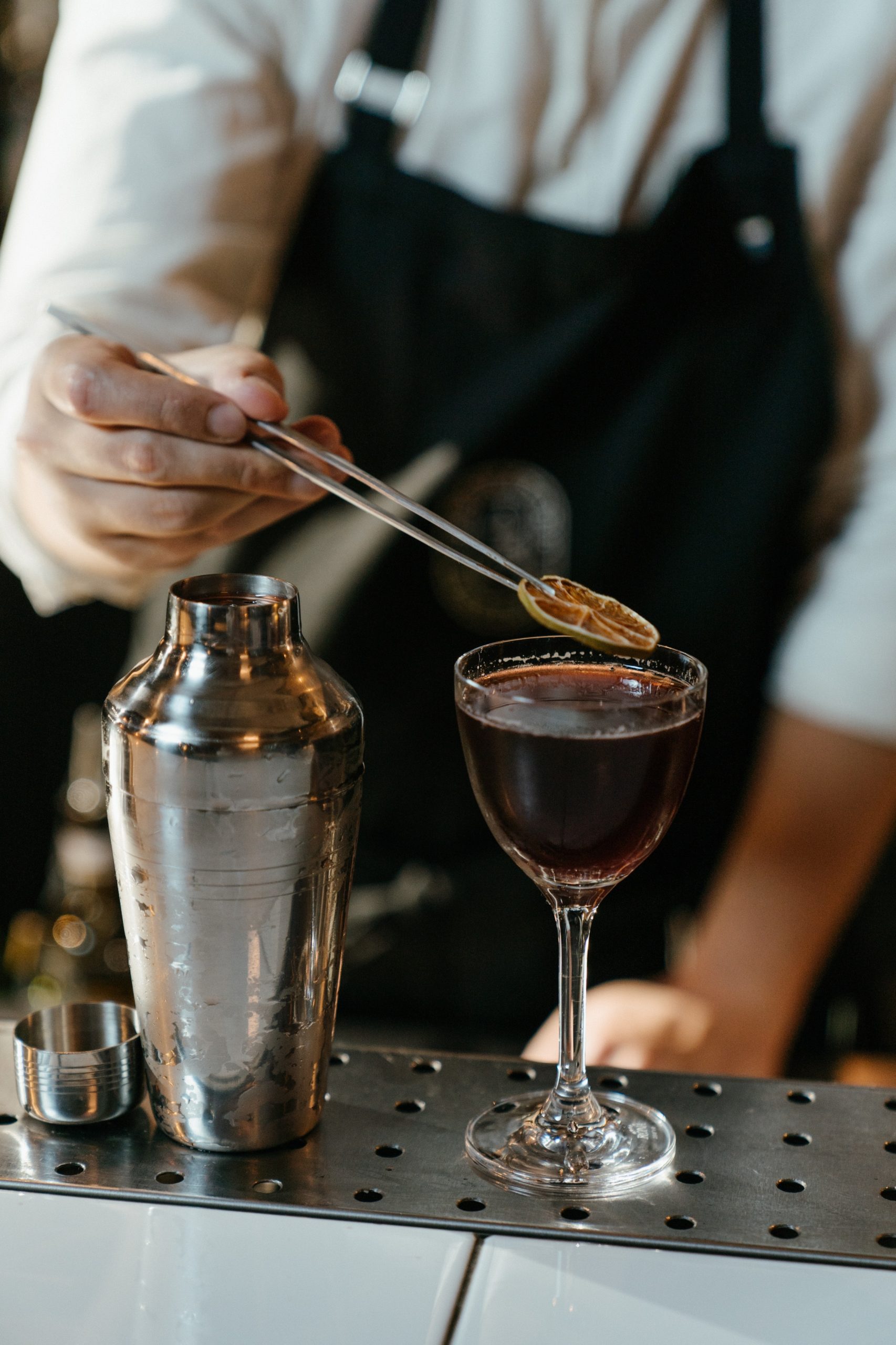 bartender adding a lime garnis to a glass of red wine using tweezers
