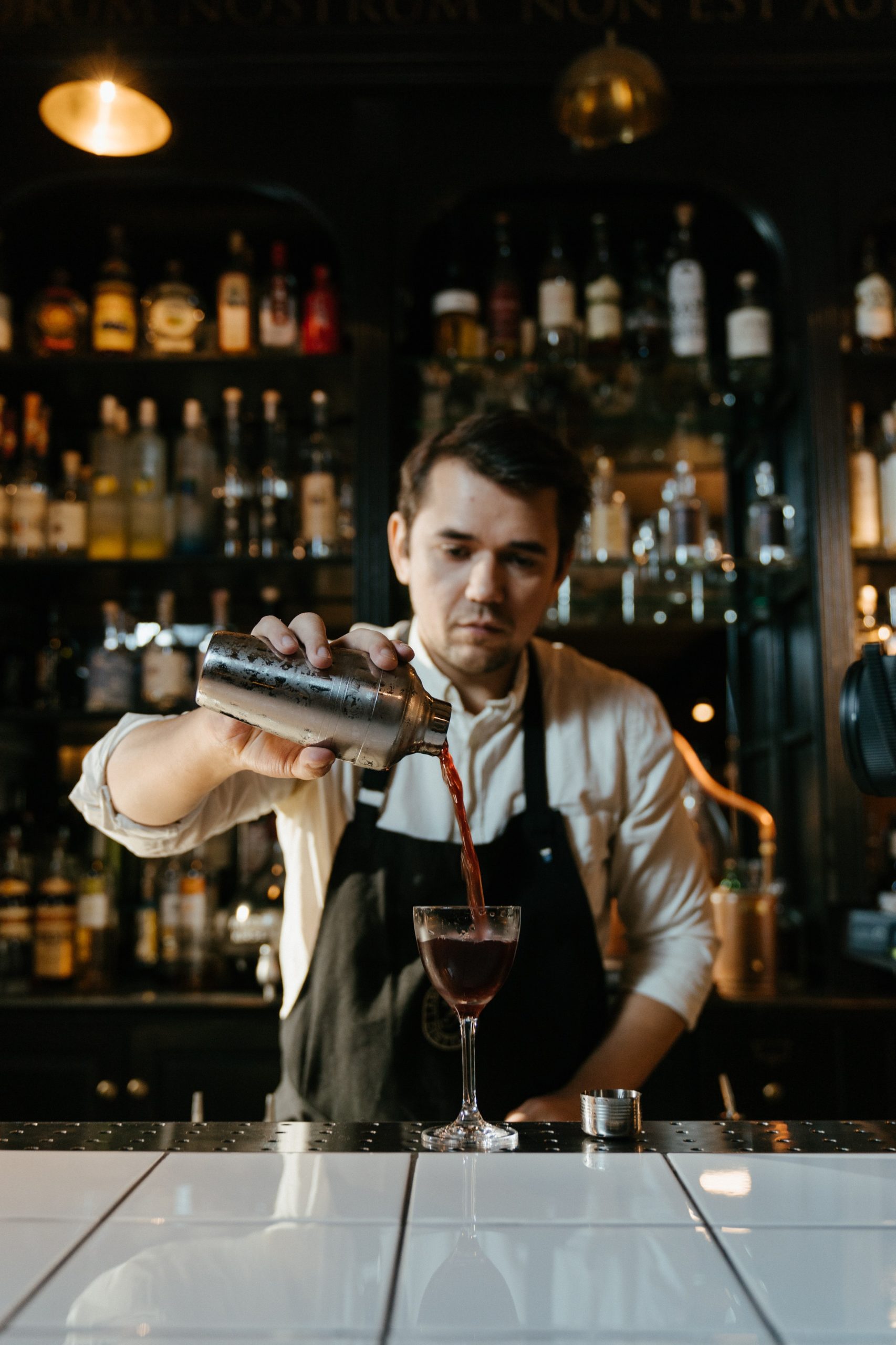 male bartender pouring a drink from a martini shaker in a bar