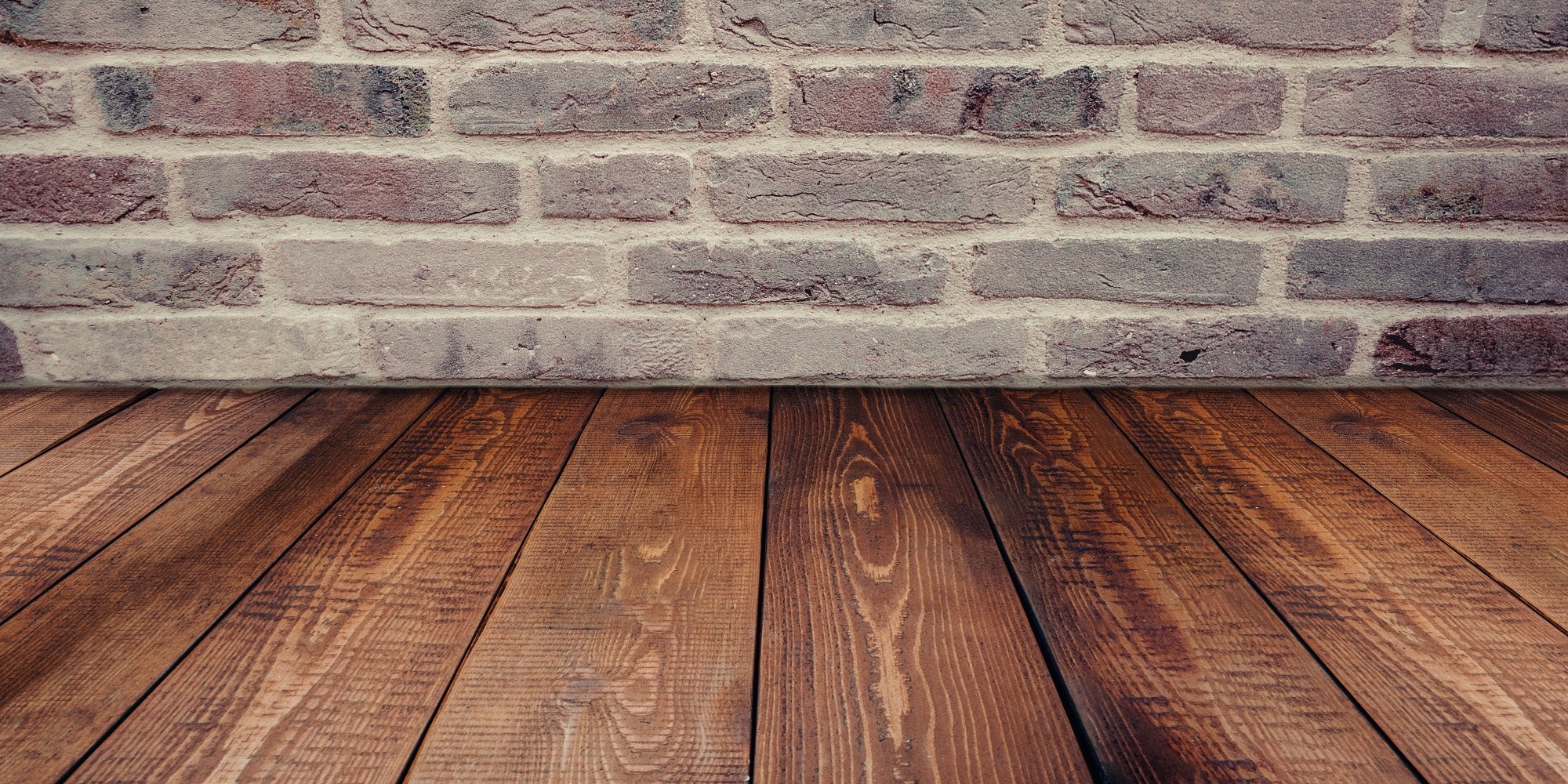 wide stained wood plank flooring against grey brick wall