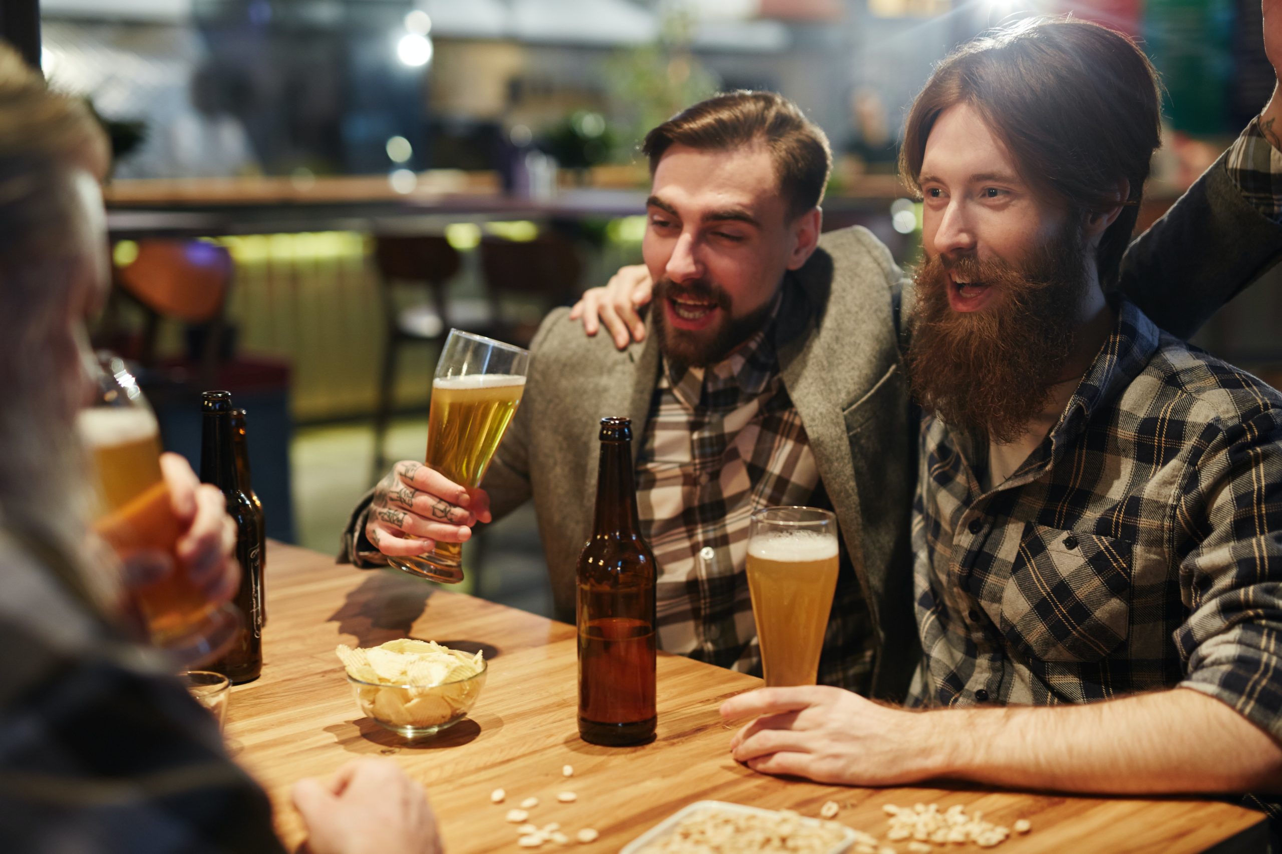 man with mustache and man with beard having a good time at a table drinking beer