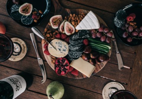 fancy cheese, crackers, fruit and nuts on a round serving tray seved on a rustic wood table with wine