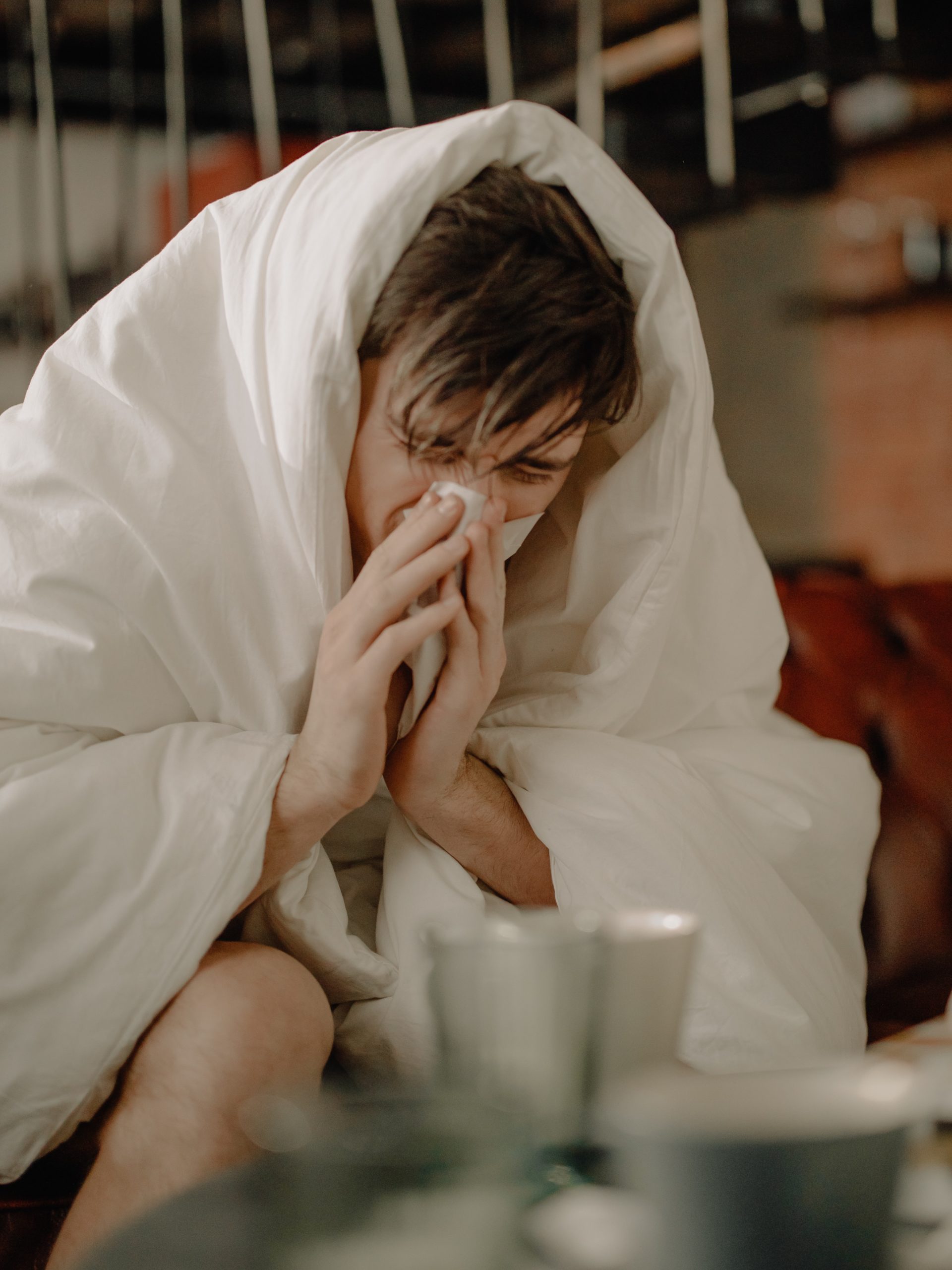 sick man wearing a blanket and blowing his nose