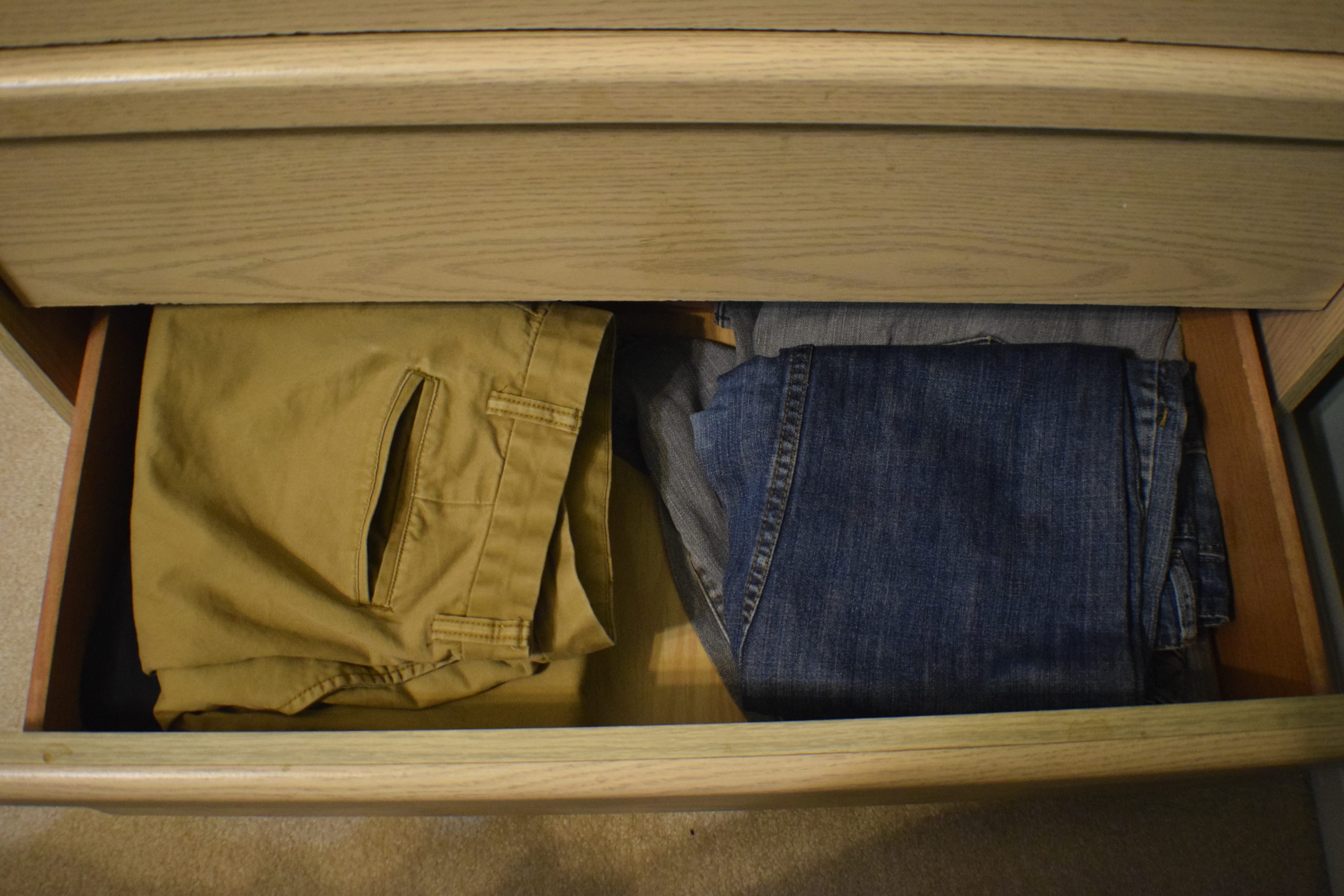 folded pants in a bottom drawer of a light wood dresser