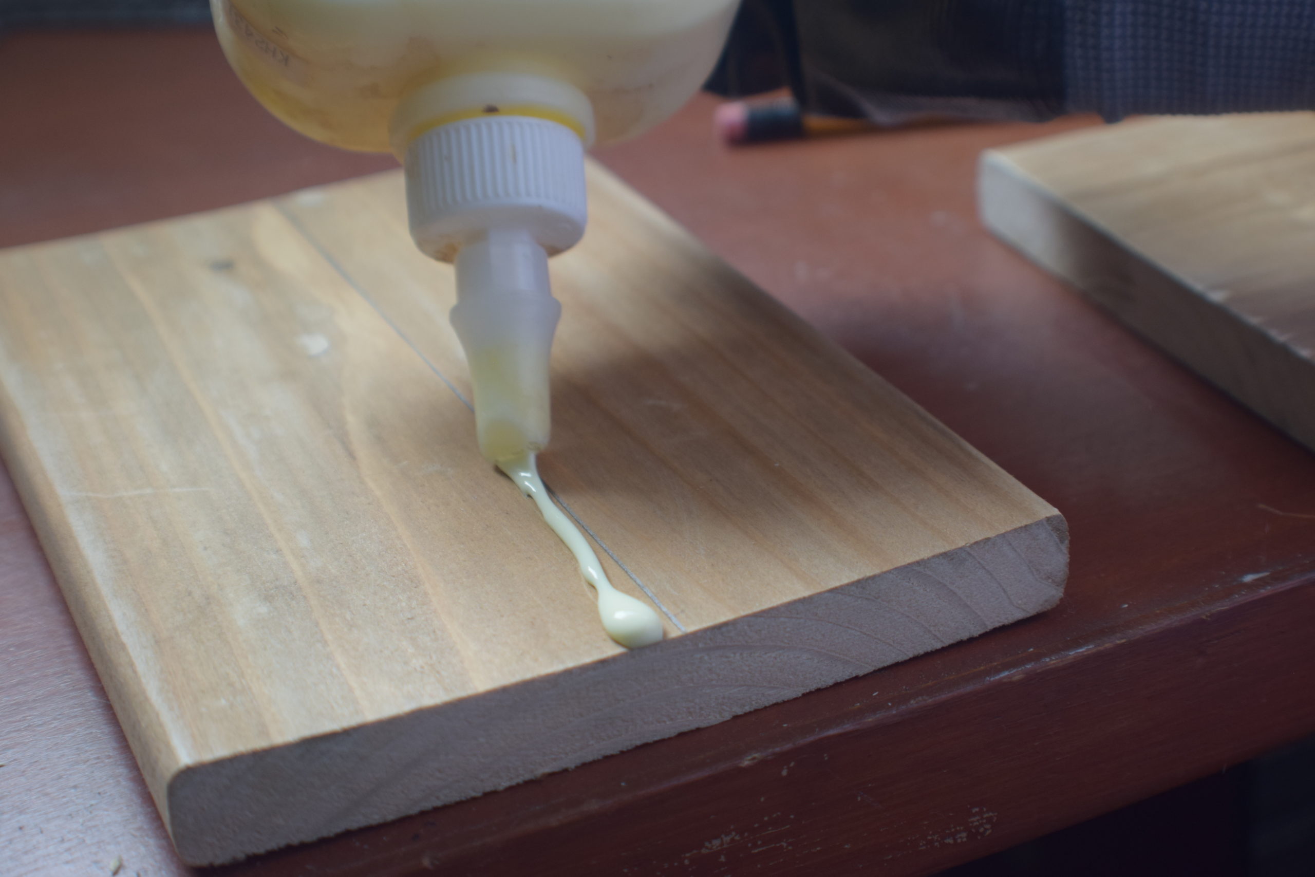 Wood glue being applied to a penciled line on wood