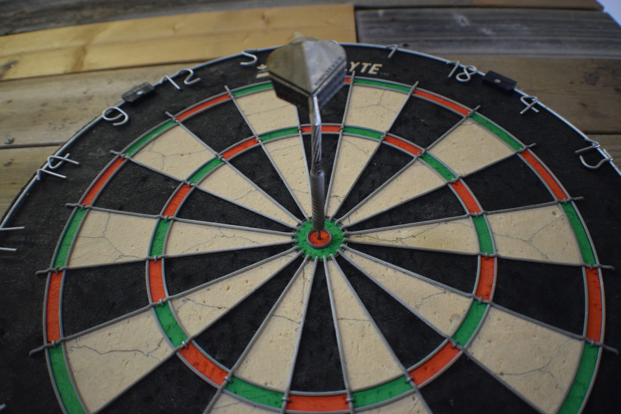 standard dartbaord on wood wall with dart in the bullseye