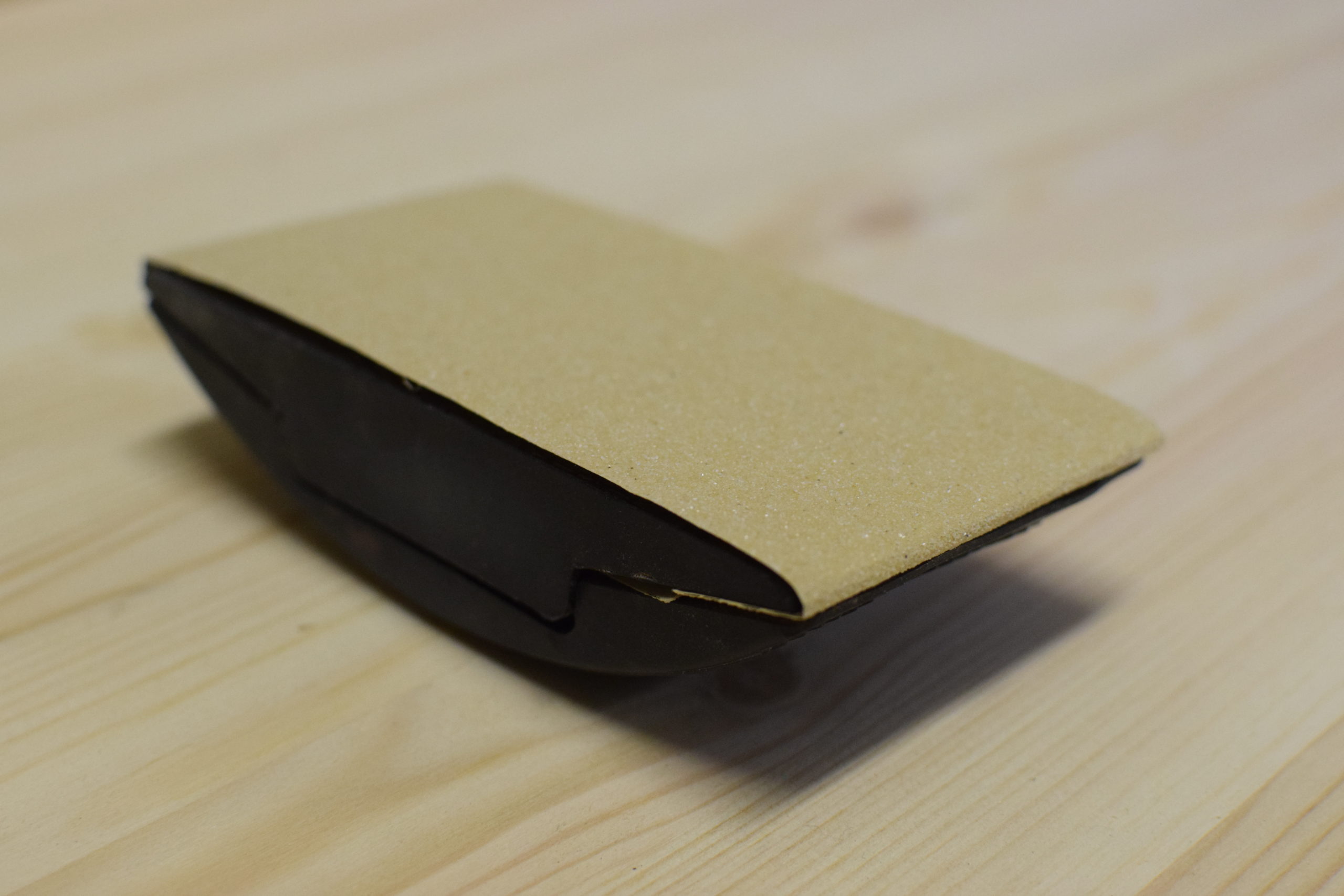 hand sanding block loaded with sand paper on a pine surface