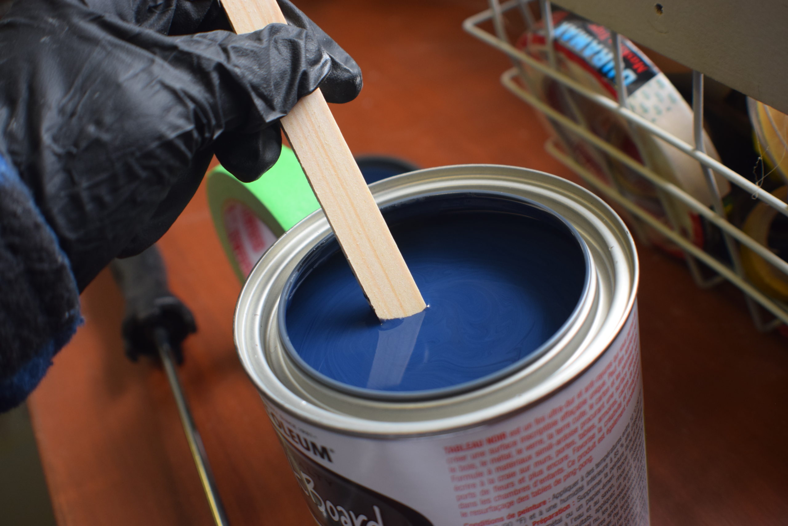 Hand with black glove stirring a can of rustoleum chalkboard paint