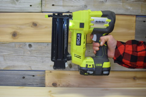 hand holding green and black Ryobi airstrike nail gun on a wood background