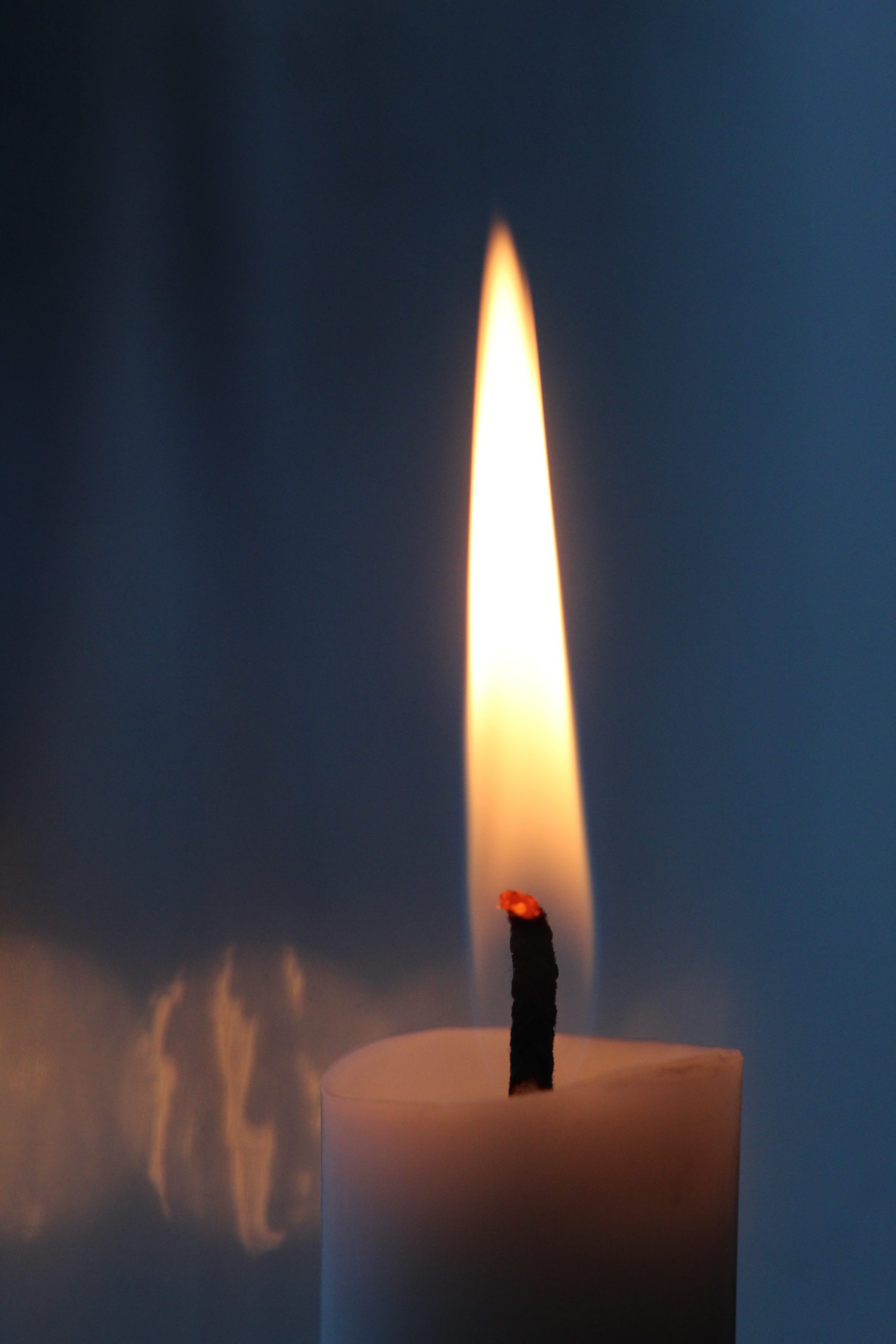 long candle flame on white wax with blue background