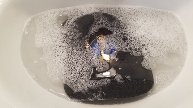 black baseball cap submerged in a sink of soapy water