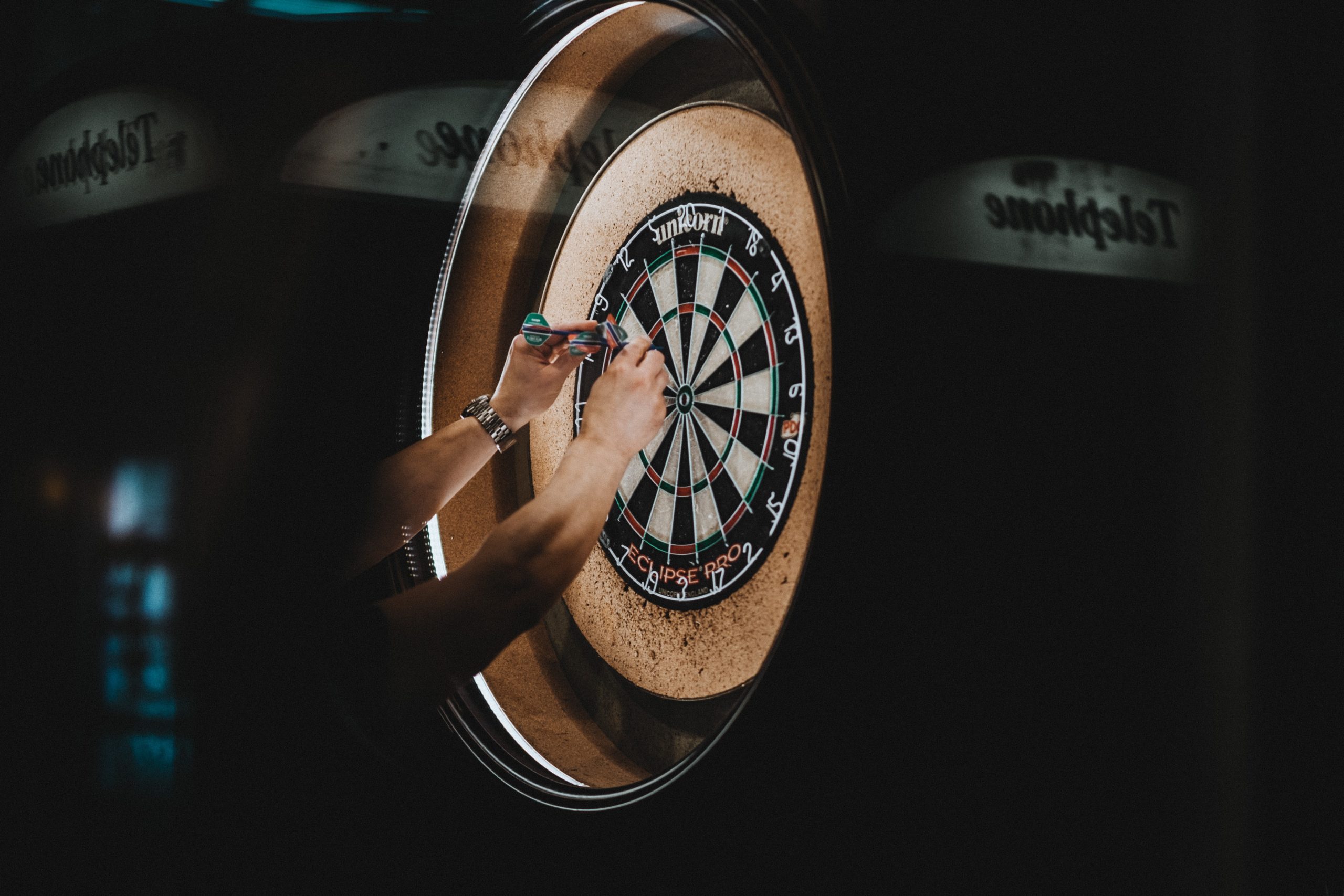 hands grabbing darts from dart board in dark room