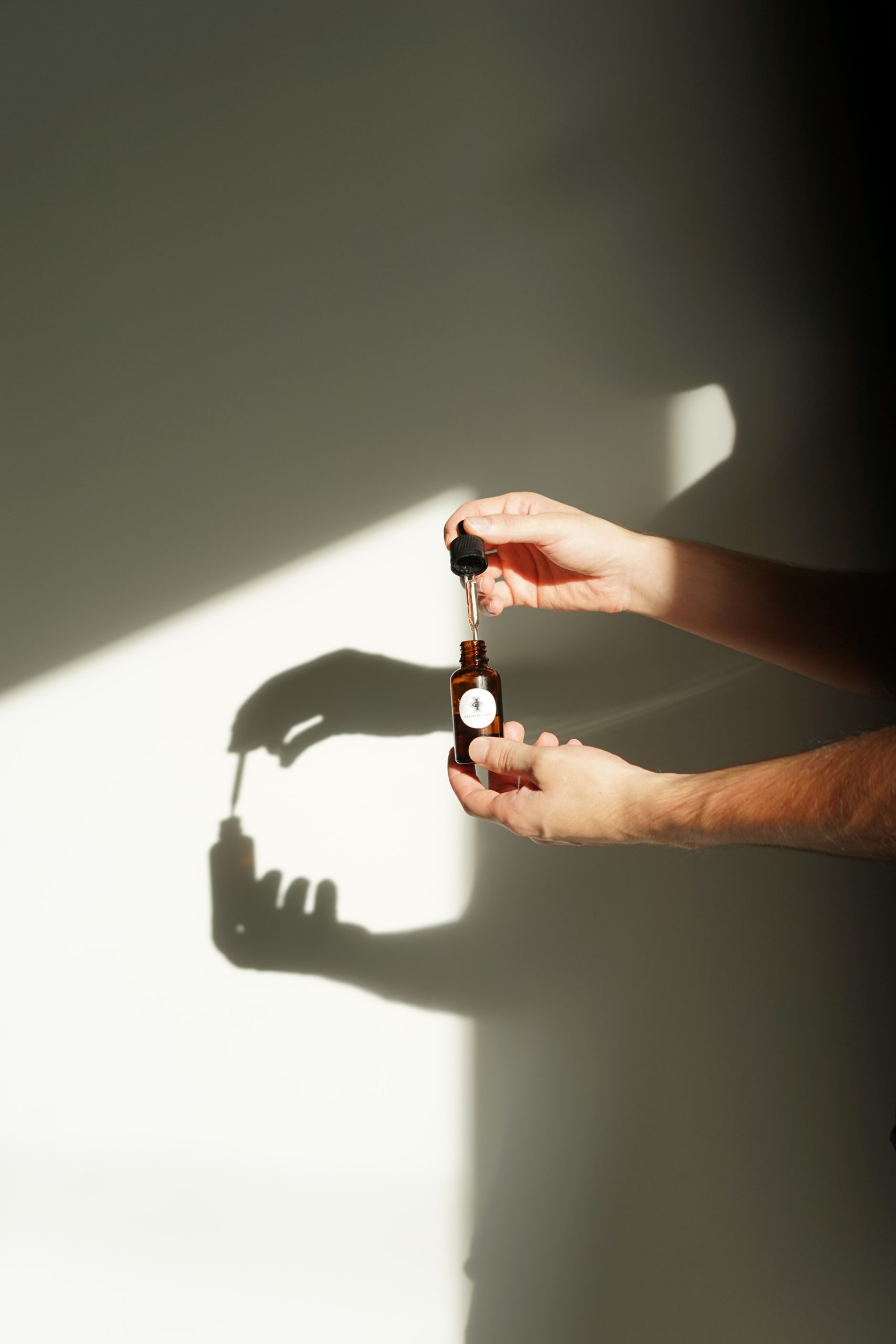 man hands holding a bottle of essential oil in front of a wall with a shaddow