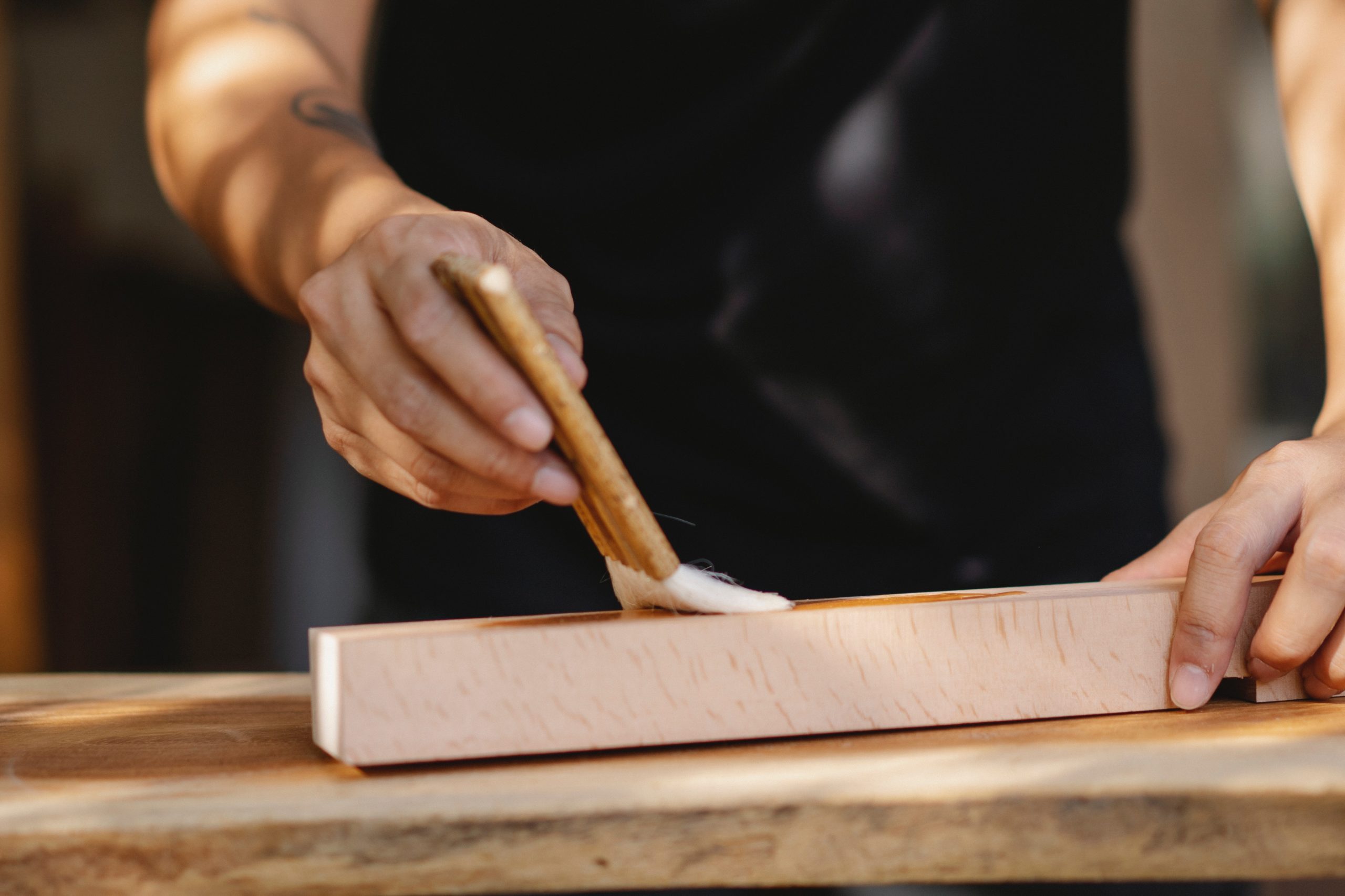 man applying Lacquer iwth a paint brush on a wood surface outside