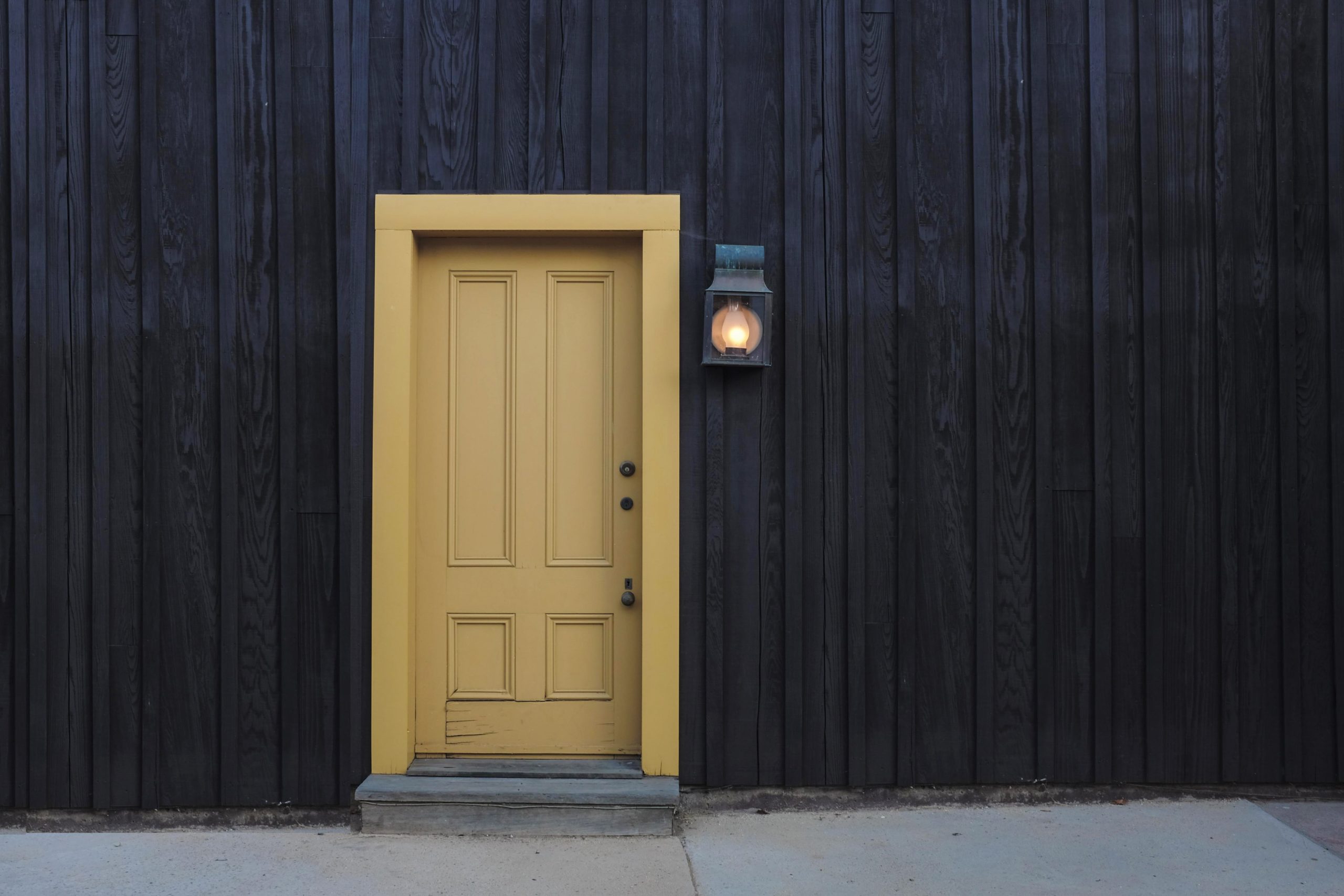 Yellow exterior front door on a dark siding building with the exterior light turned on