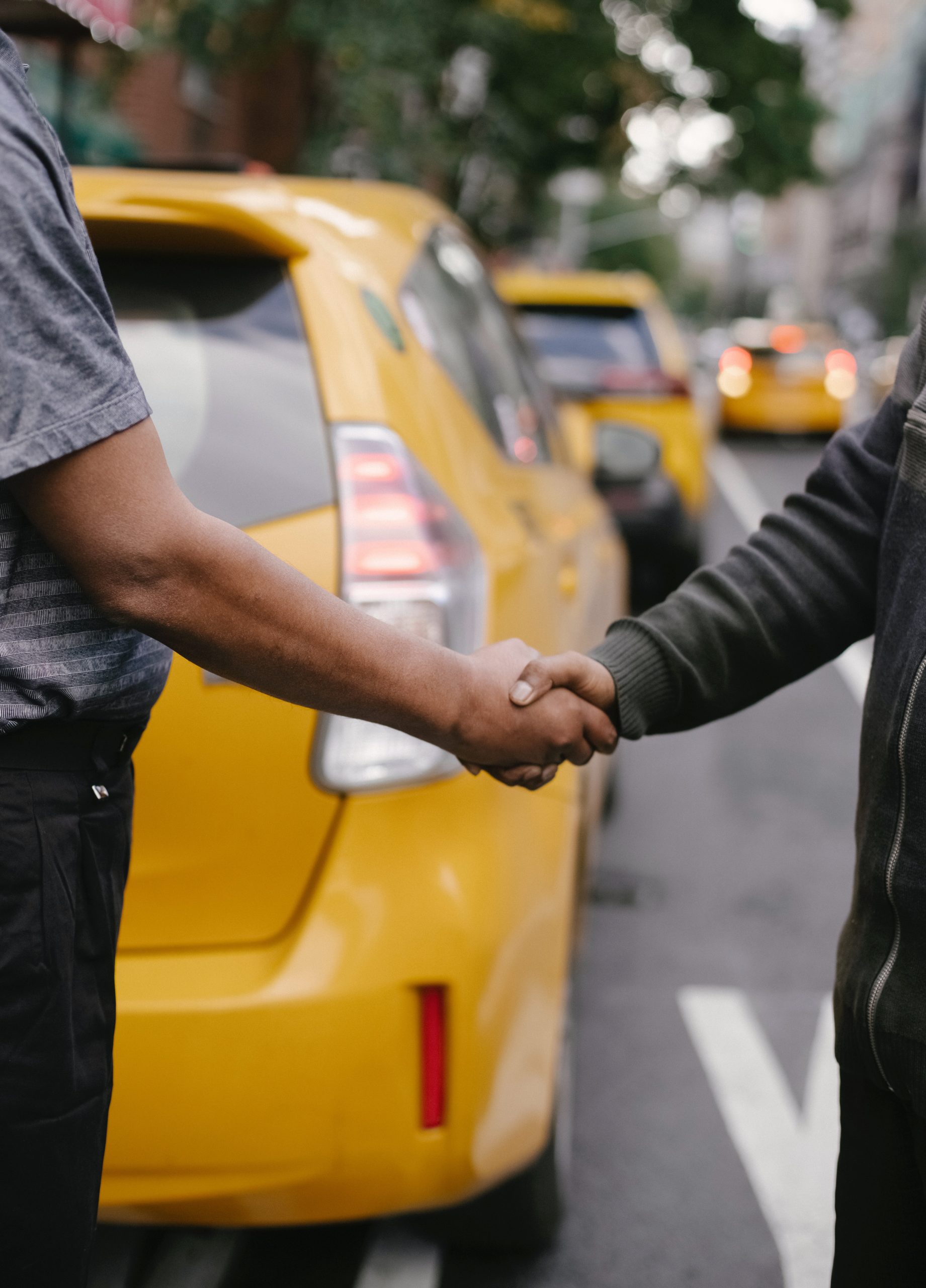 2 men shaking hands on a street with yellow parked cars