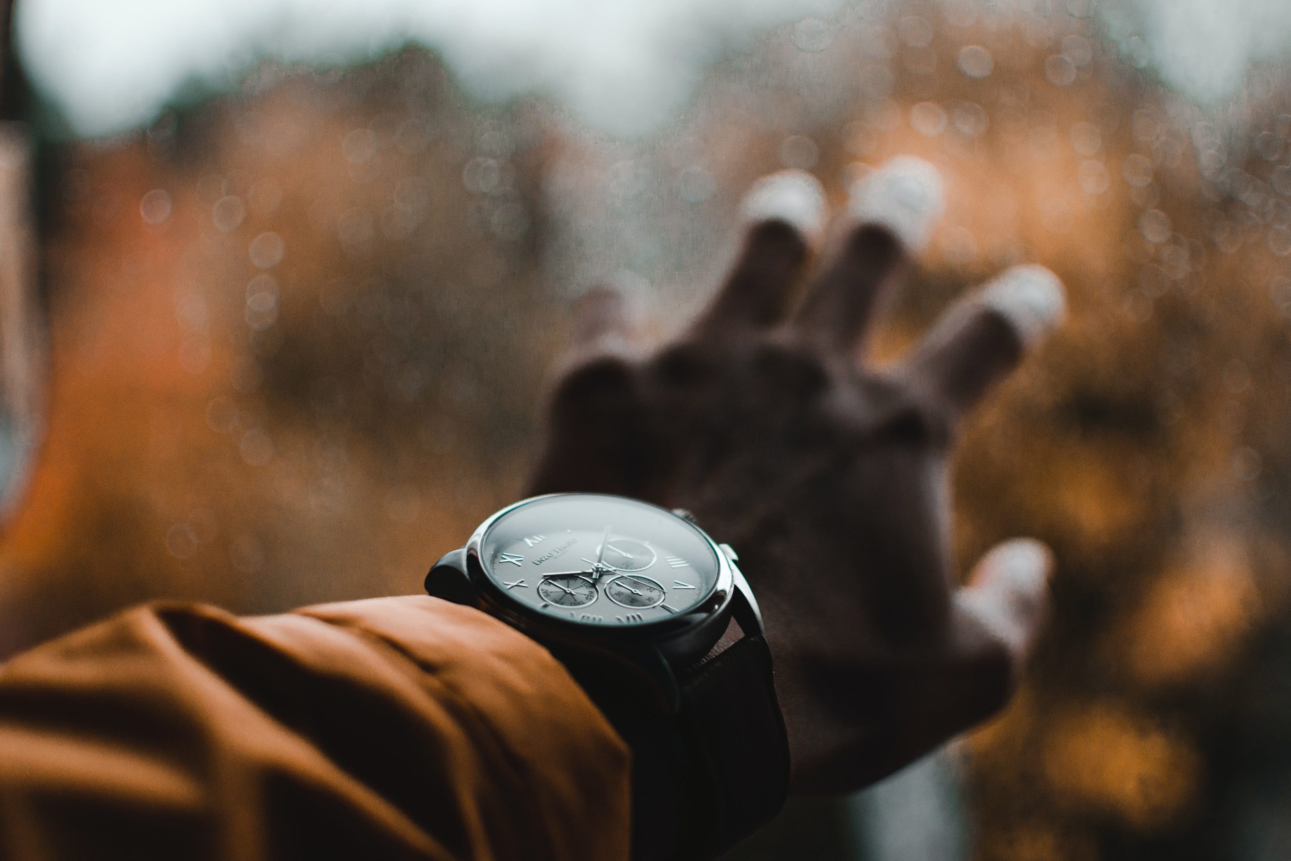 man wearing a large watch with yellow jacket holding his hand against a window in the fall