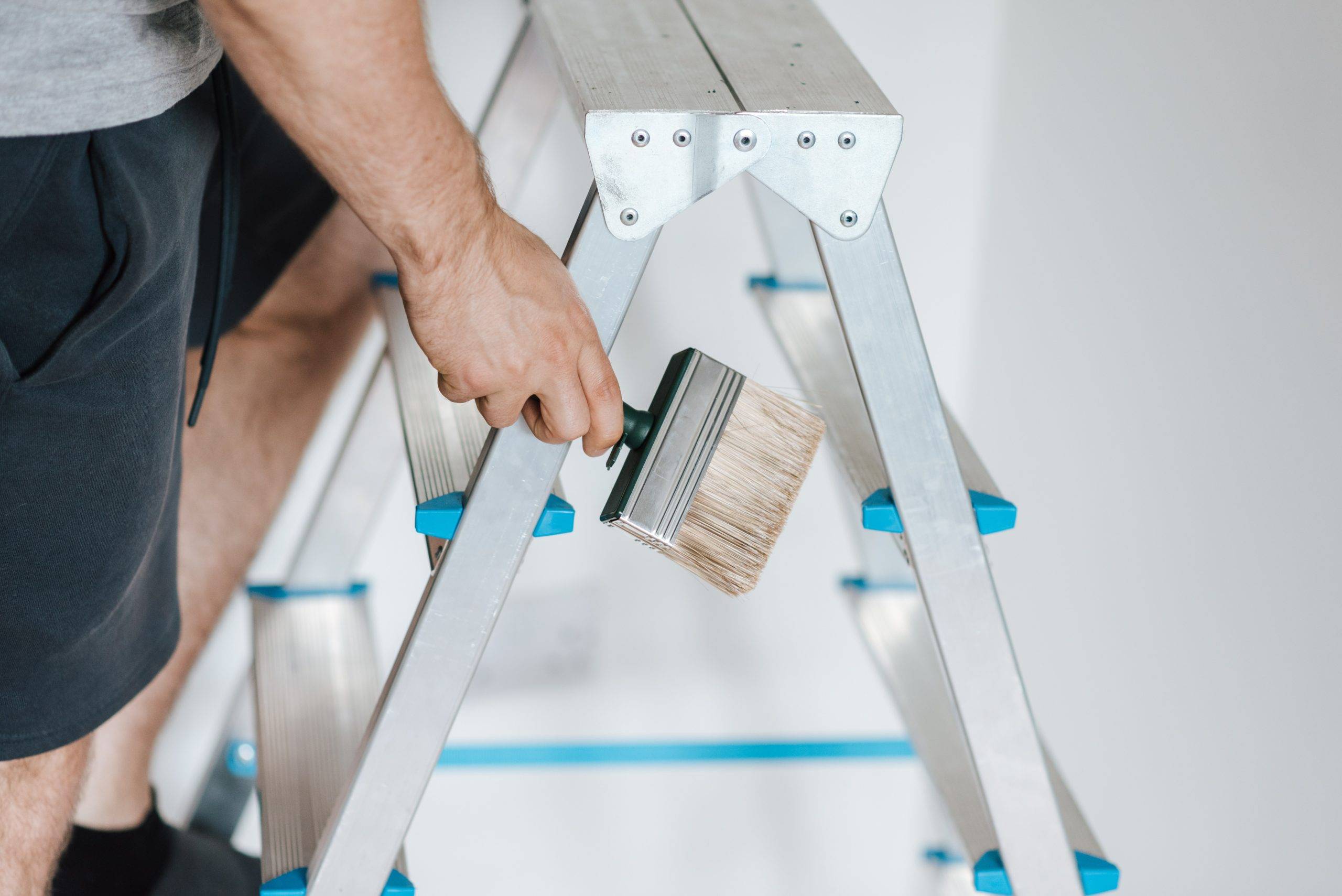 Guy holding a paint brush while climbing a ladder