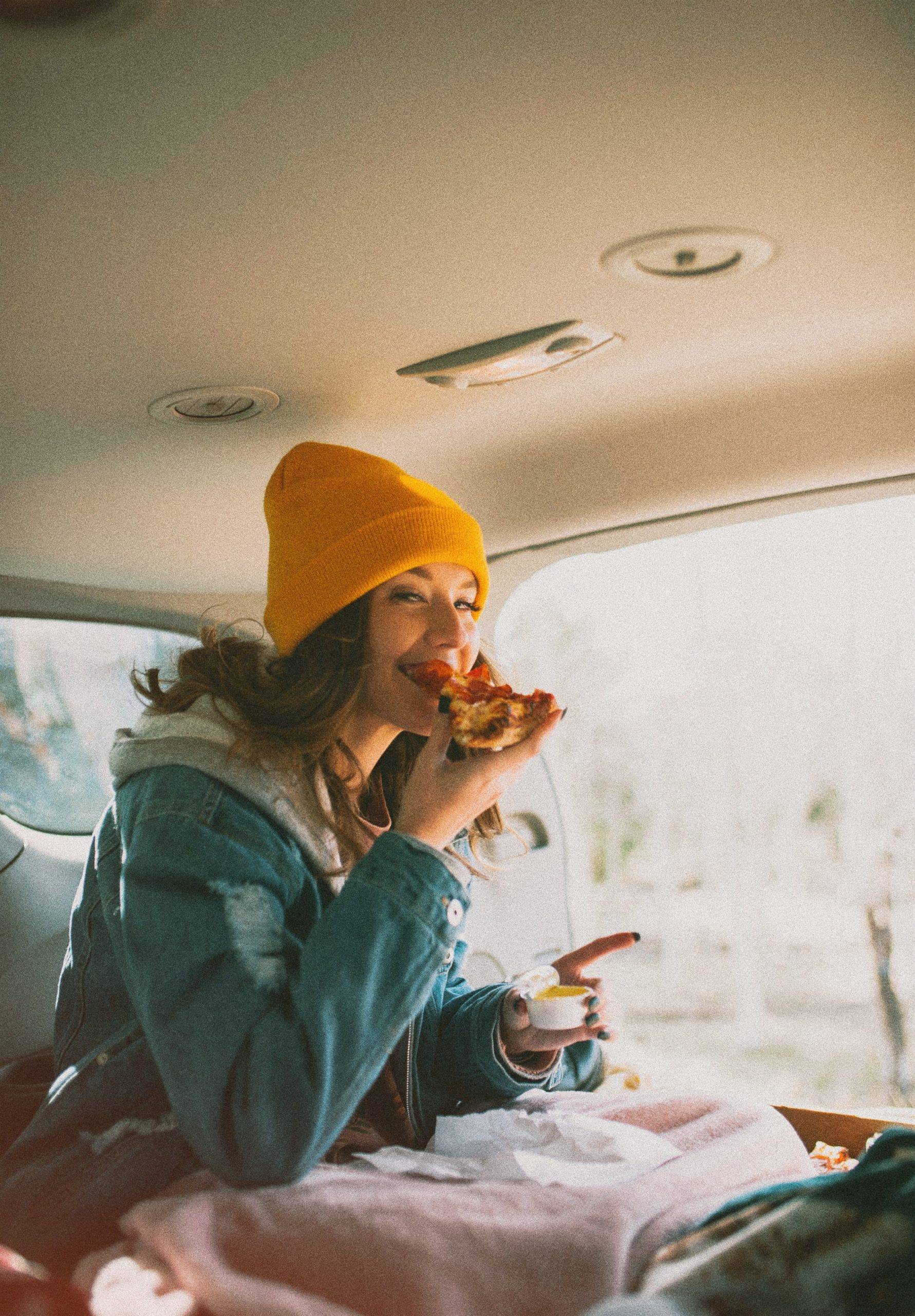 Woman in yellow beanie eating pizza in the car