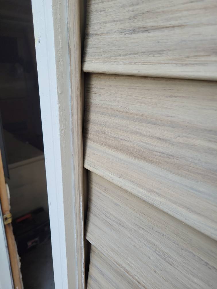 Closeup showing siding slid behind the brick molding of a vinyl siding near a door.