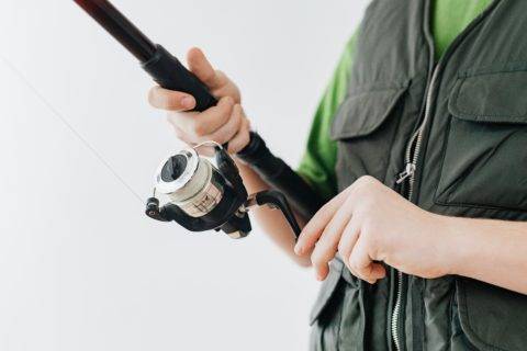 person in fishing vest casting spinning reel
