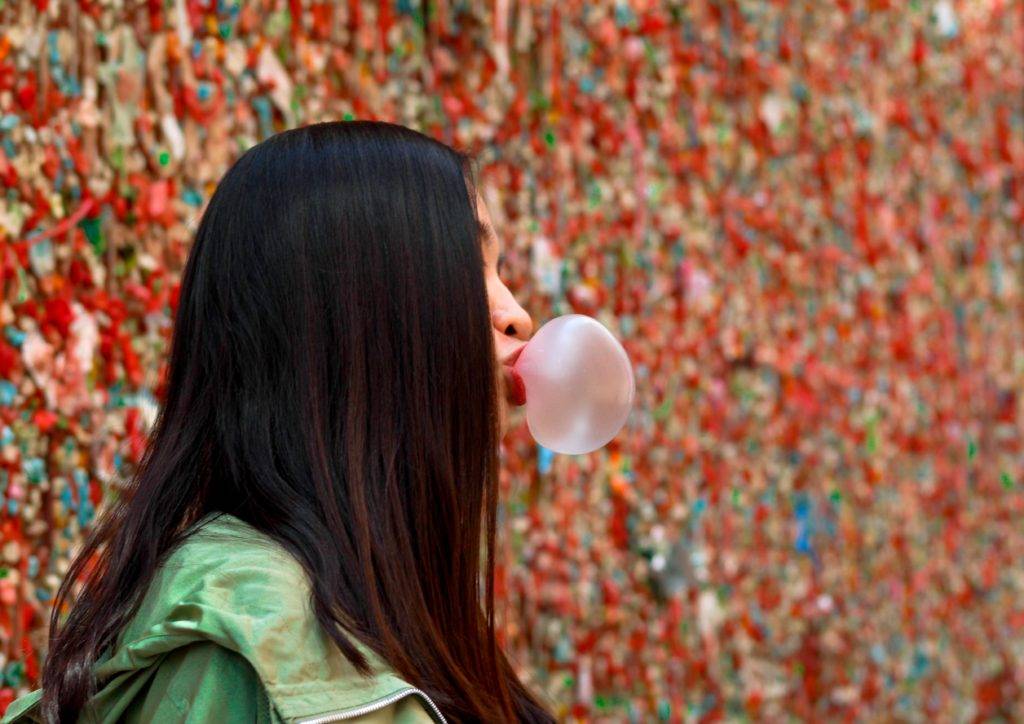 girl in front of a gum wall blowing a bubble