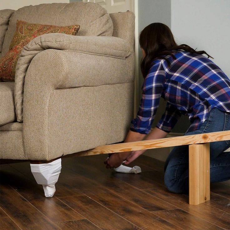 Couch is supported up by a piece of lumber as a person fits the socks to the couch's feet.