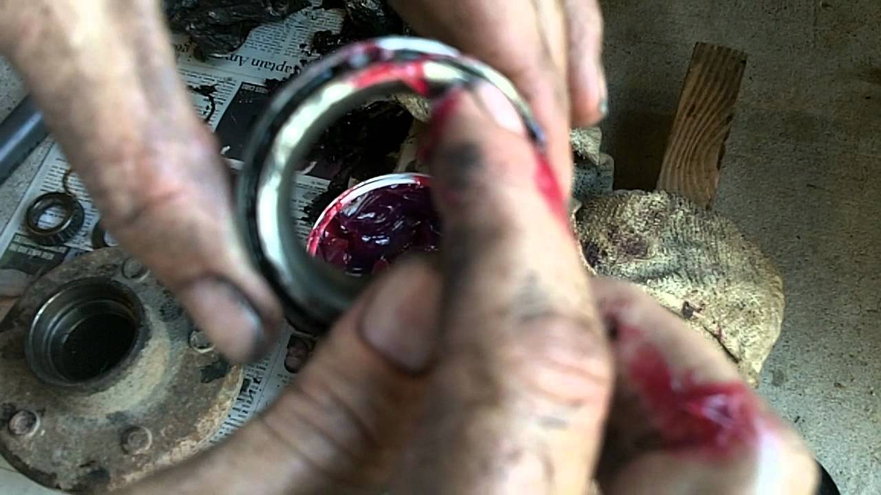 Hands are applying grease to a trailer bearing.